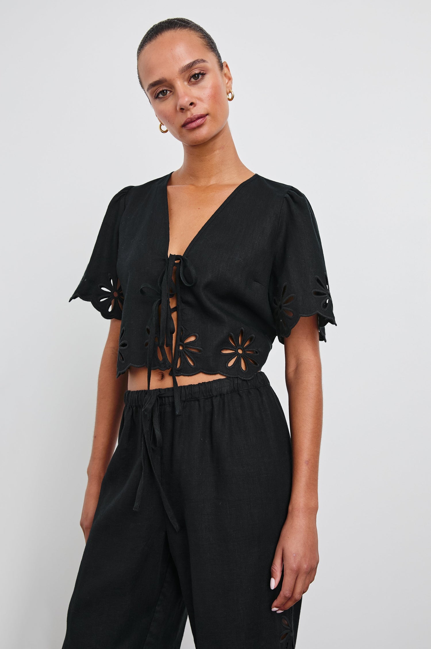 Pari Short-Sleeve Cropped Top with V Neck, Front Tie Closures, and Floral Eyelets in Black Eyelet Colorway - Front View Featured on Model 