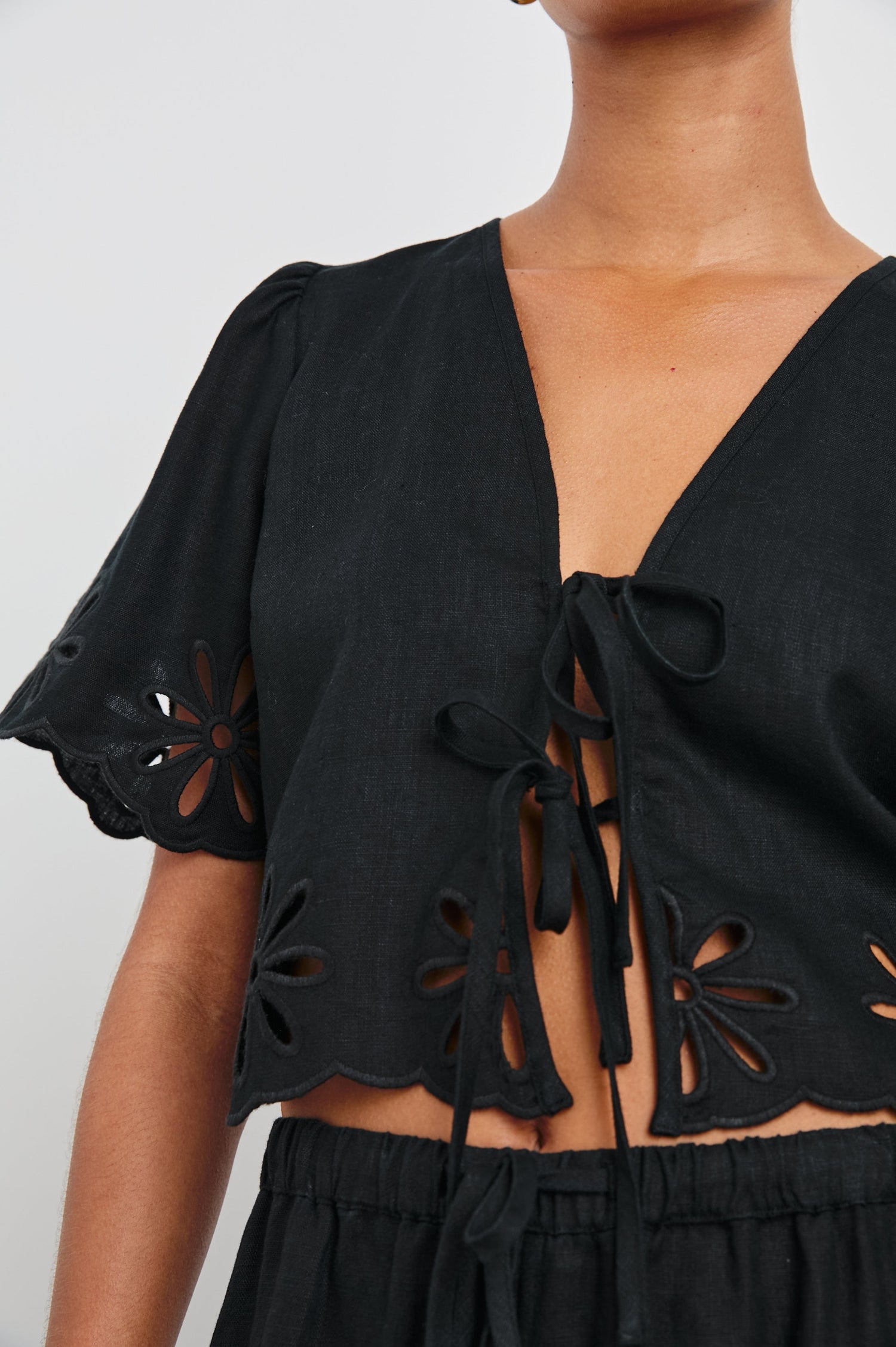 Pari Short-Sleeve Cropped Top with V Neck, Front Tie Closures, and Floral Eyelets in Black Eyelet Colorway - Front View Featured on Model 