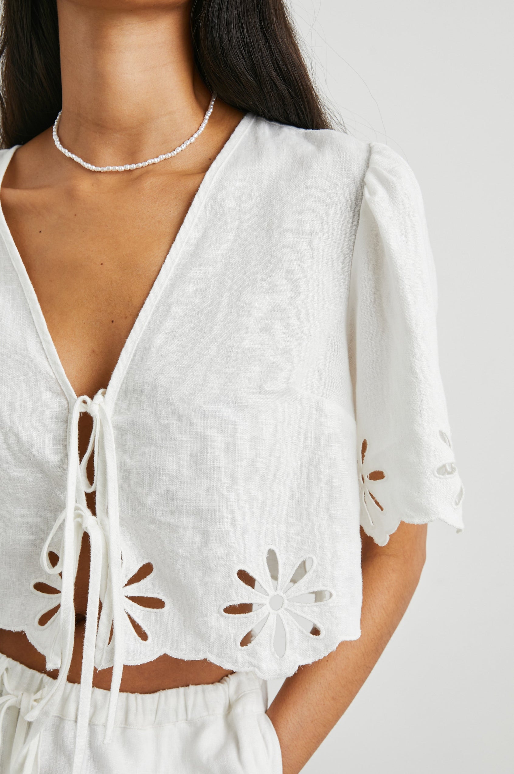 Pari Short-Sleeve Cropped Top with V Neck, Front Tie Closures, and Floral Eyelets in White Eyelet Colorway - Front View Featured on Model 