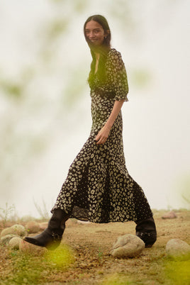 Woman in a floral dress and black boots standing in a natural setting with blurred background
