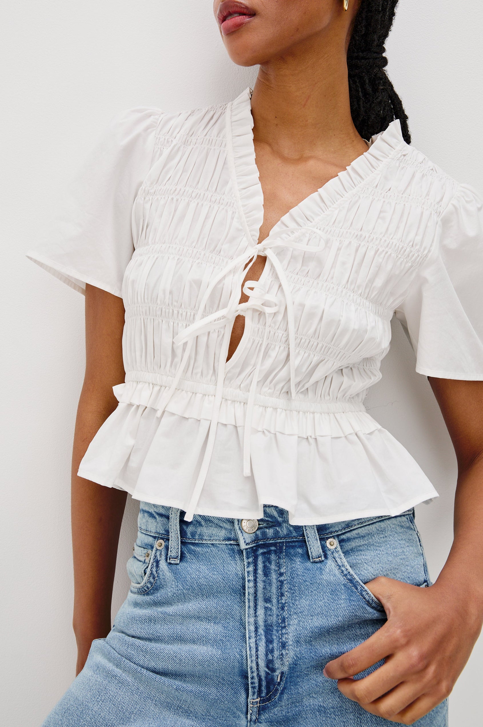 Portia V-Neck Tie Front Top with Short Puff Sleeves and a Ruffled Peplum Hem in White Colorway. Front Detailed View Shown on Model.