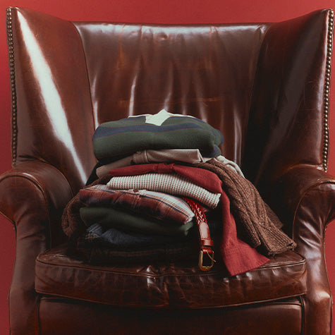 A stack of folded clothing and a brown leather armchair against a solid red background.