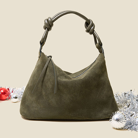 Olive green suede hobo bag with a knotted leather handle, surrounded by red and silver ornaments and tinsel on a cream background.