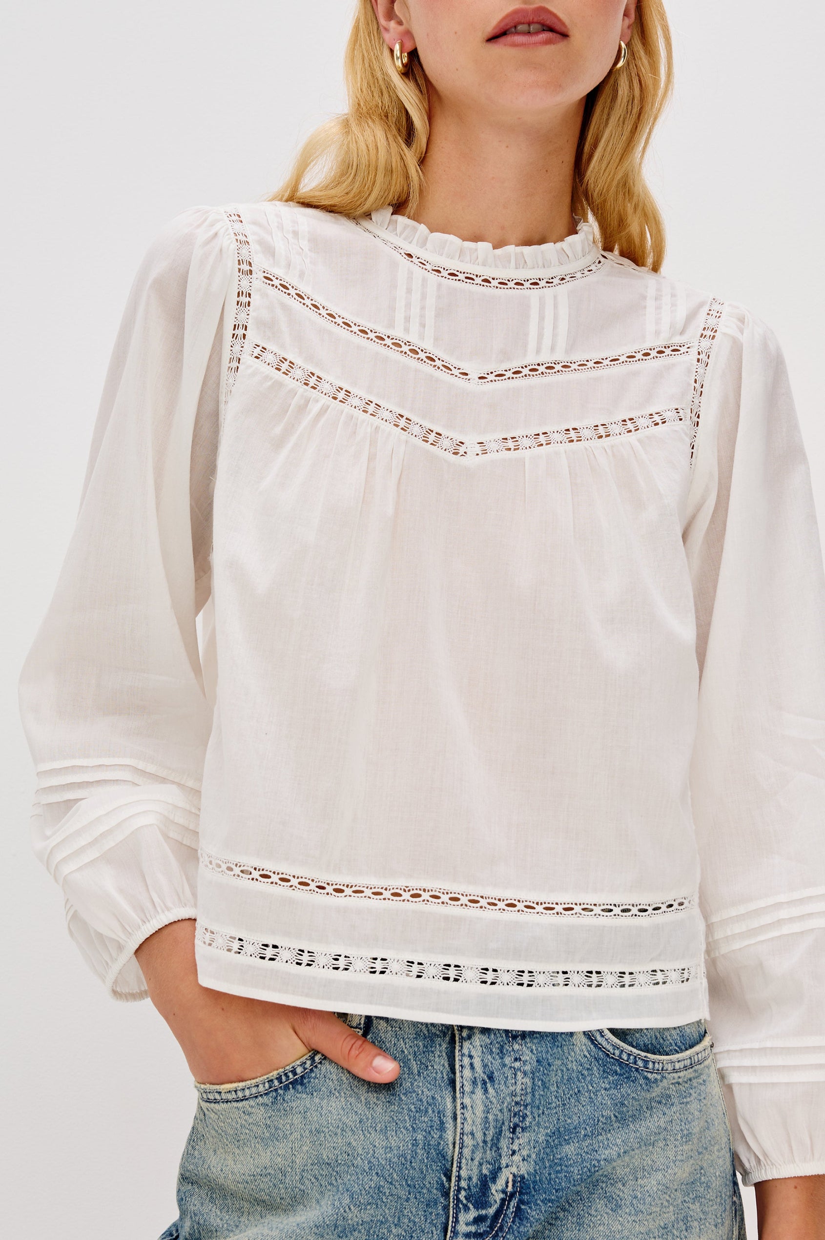 Front view of female model wearing our Reyna Top in white, close up of details. This is a long sleeve crewneck baby doll blouse, with ruffles at the collar. 