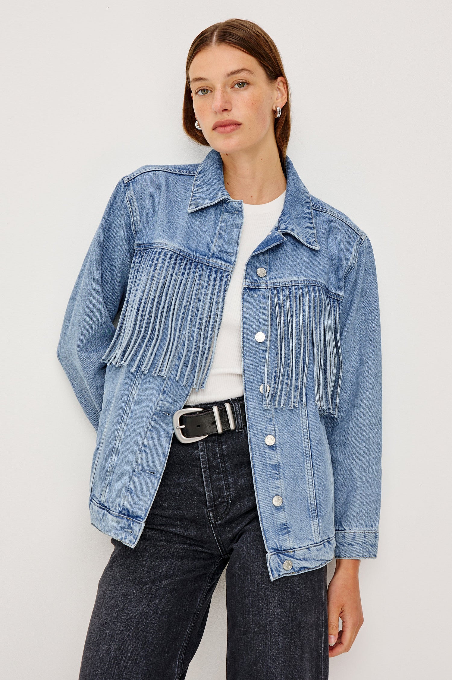 The Rodeo is button front collared denim jacket with side pockets and fringe along front yoke in Indigo Cowboy colorway, a medium blue wash. Front view featured on model.