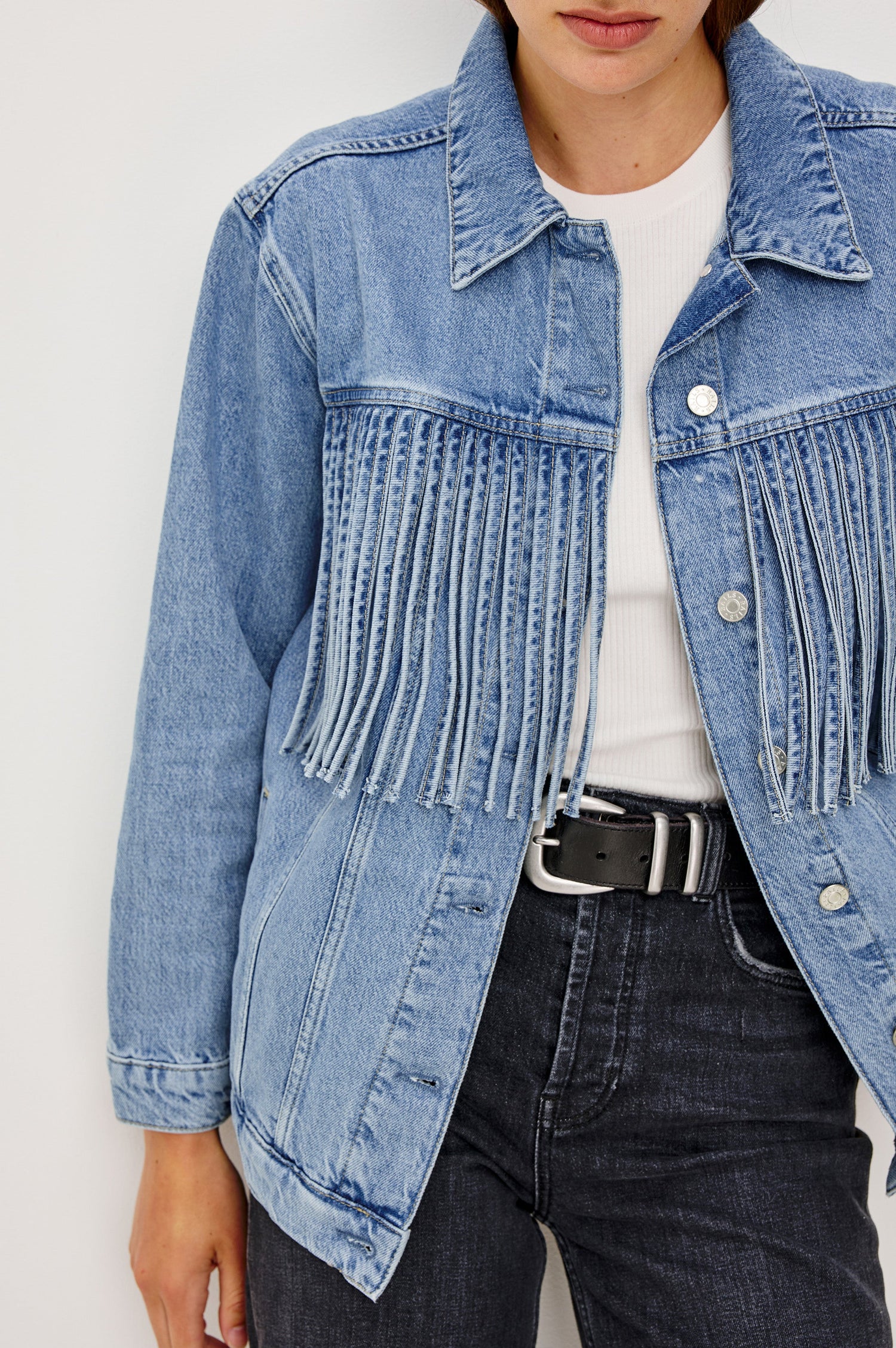 The Rodeo is button front collared denim jacket with side pockets and fringe along front yoke in Indigo Cowboy colorway, a medium blue wash. Front detail view featured on model.