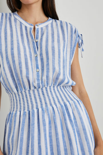 Samina Above-Knee Sleeveless Dress with drawstrings at the Sleeve Openings, Buttons along the Bodice, A Cinched Waist and a Tiered Skirt in Casablanca Stripe Colorway, with blue vertical stripes on white - Front View Featured on Model 