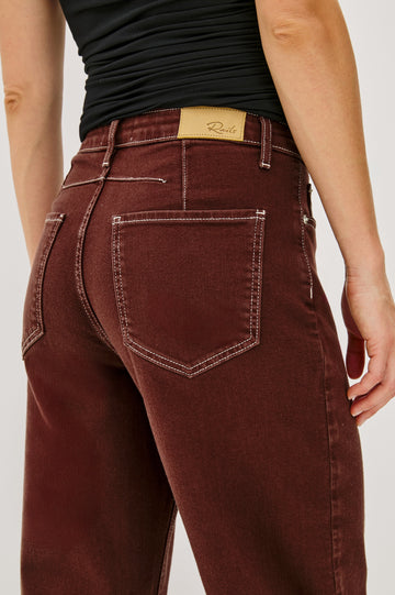 The Samo is a denim barrel leg jean, it features a low-slung fit in light-stretch denim with darting details and a subtle curved seam in Chocolate Contrast Stitch colorway. Front view featured on model.