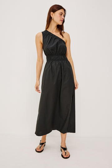 Selani Midi Dress With an Asymmetrical Neckline, Mid-Thigh Slide Slit and Cinched Waistband in Black Colorway - Front Full Body View Featured on Model