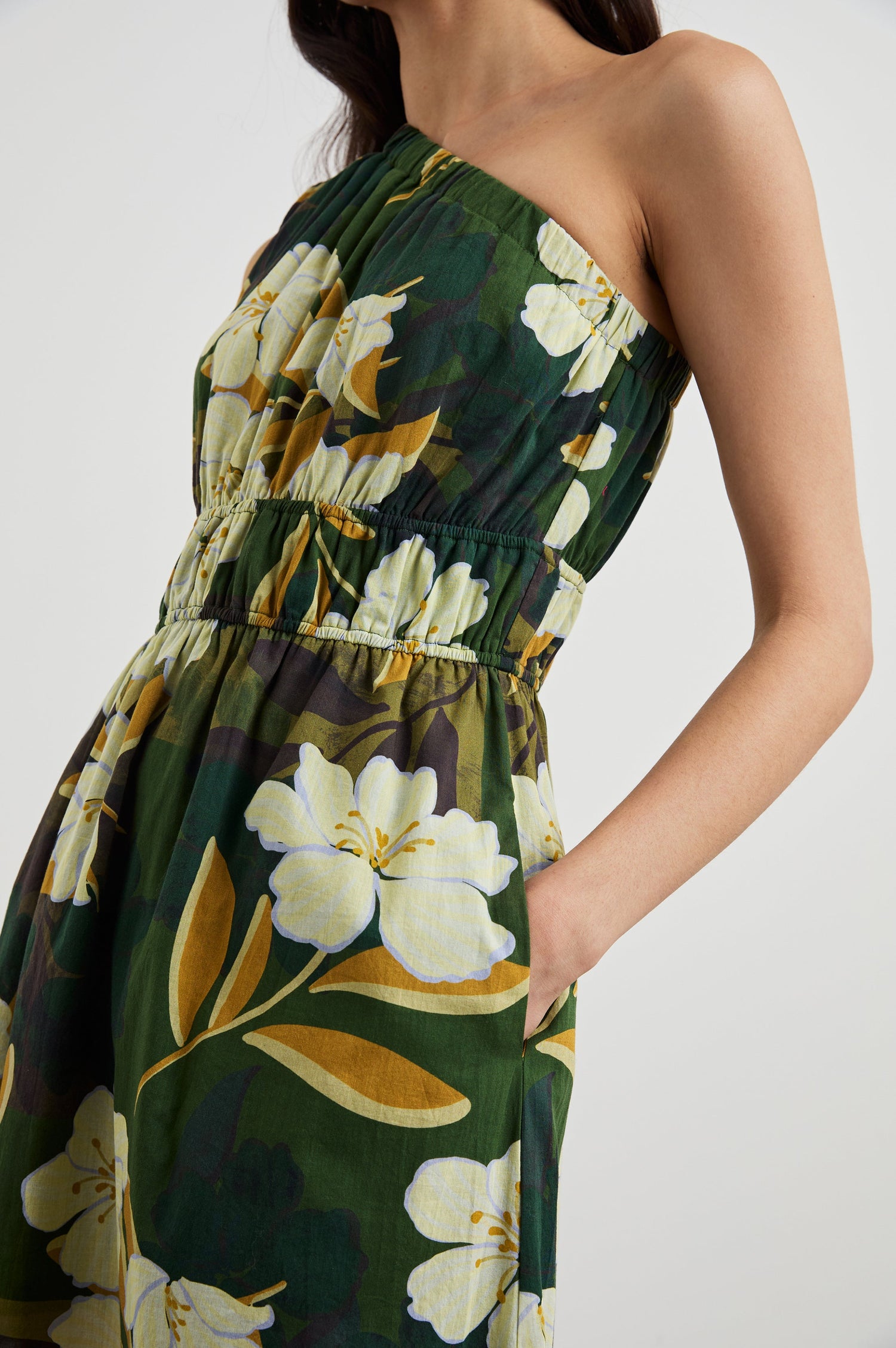 Selani Midi Dress With an Asymmetrical Neckline, Mid-Thigh Slide Slit and Cinched Waistband in Plumerias Colorway, with Ivory and Gold Plumerias on Dark Green  - Side View Featured on Model