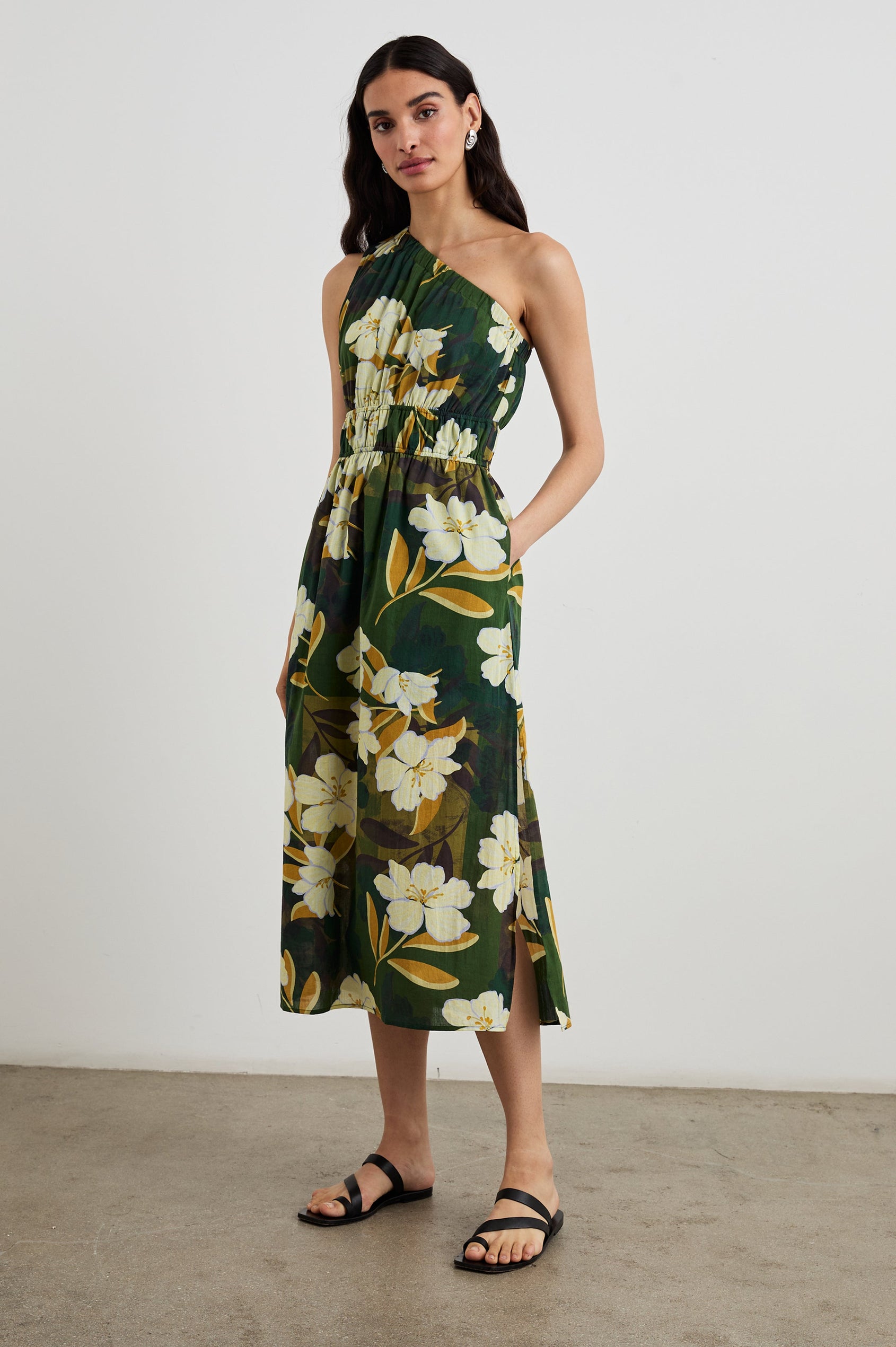 Selani Midi Dress With an Asymmetrical Neckline, Mid-Thigh Slide Slit and Cinched Waistband in Plumerias Colorway, with Ivory and Gold Plumerias on Dark Green  - Front Full Body View Featured on Model