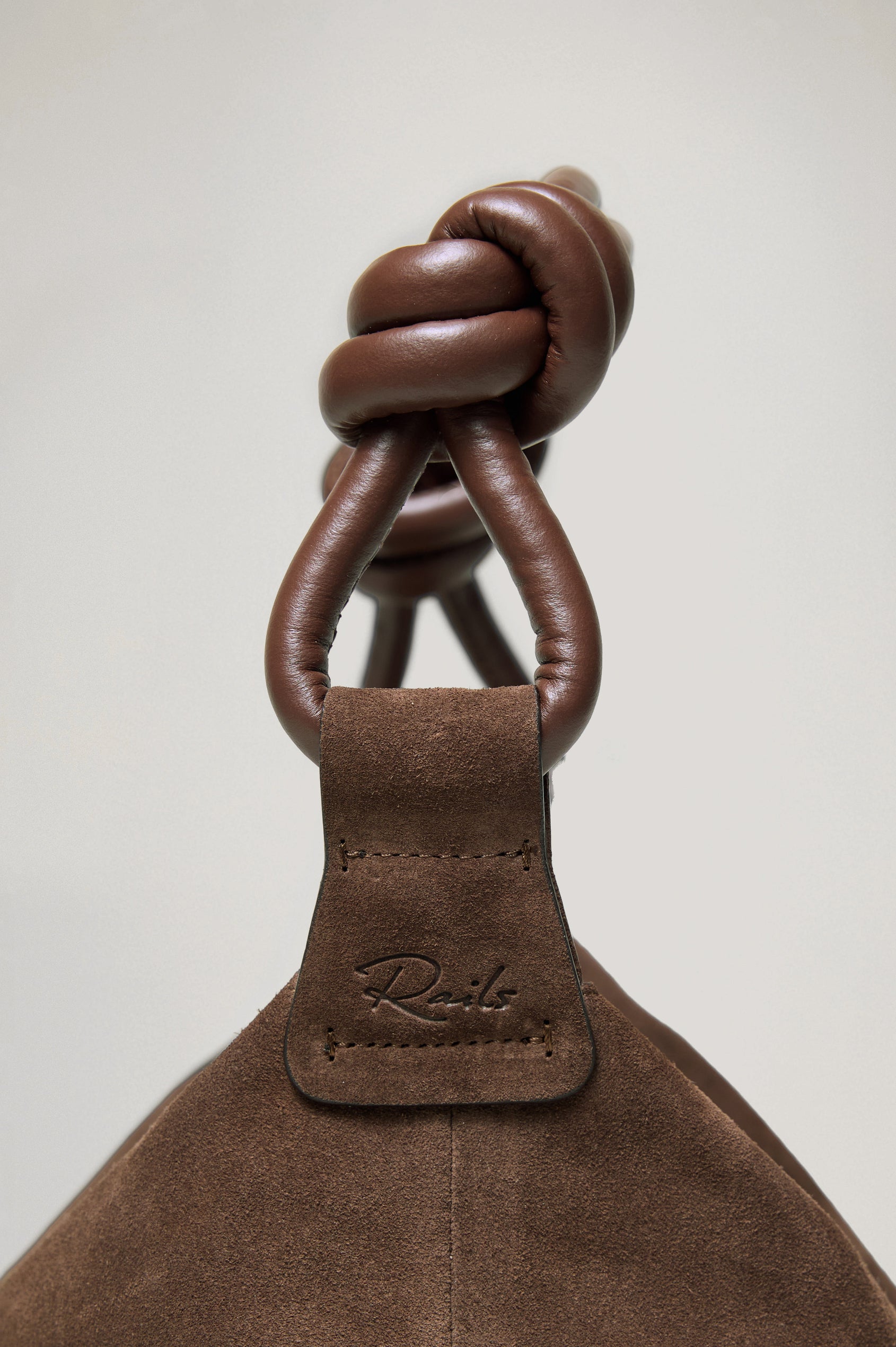 The Siena is a true slouchy hobo bag, crafted from smooth leather with a knotted top strap and a zip closure finished with a fringed tassel. In Espresso Suede Colorway. Detailed view of strap featured.