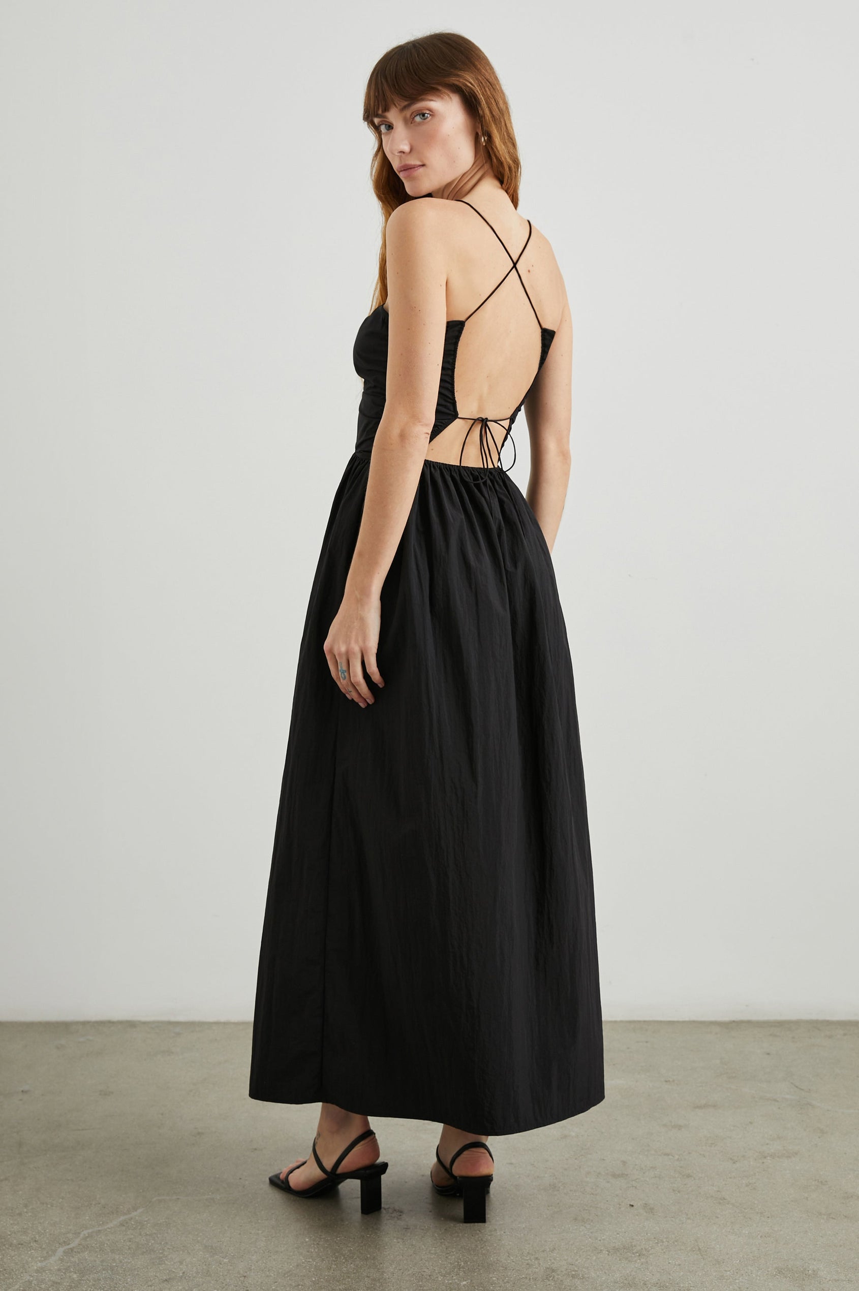 Silvia Sleeveless Maxi Dress with Spaghetti Straps with a Lower Back Tie, an Open Back, and Cutouts Along the Center of the Bodice in Black Nylon Colorway - Back Full Body View Featured on Model