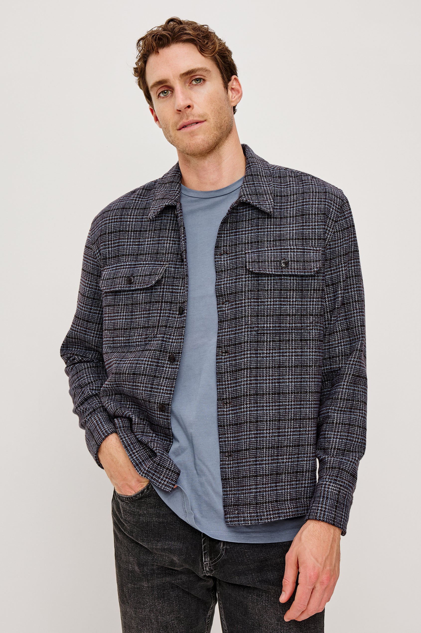 Stellan is a shirt jacket made from heavy brushed cotton with a classic collar, front button closures, chest flap pockets in Cedar Bay, a blue and grey plaid colorway. Front view featured on model.