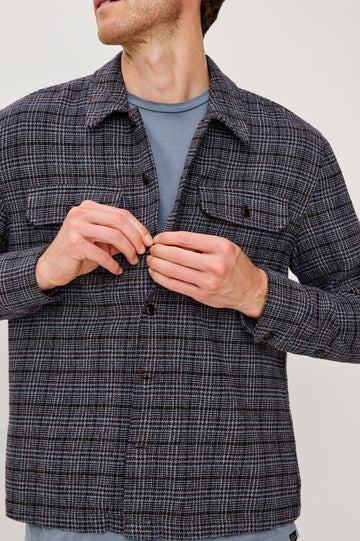 Stellan is a shirt jacket made from heavy brushed cotton with a classic collar, front button closures, chest flap pockets in Cedar Bay, a blue and grey plaid colorway. Front detail view featured on model.
