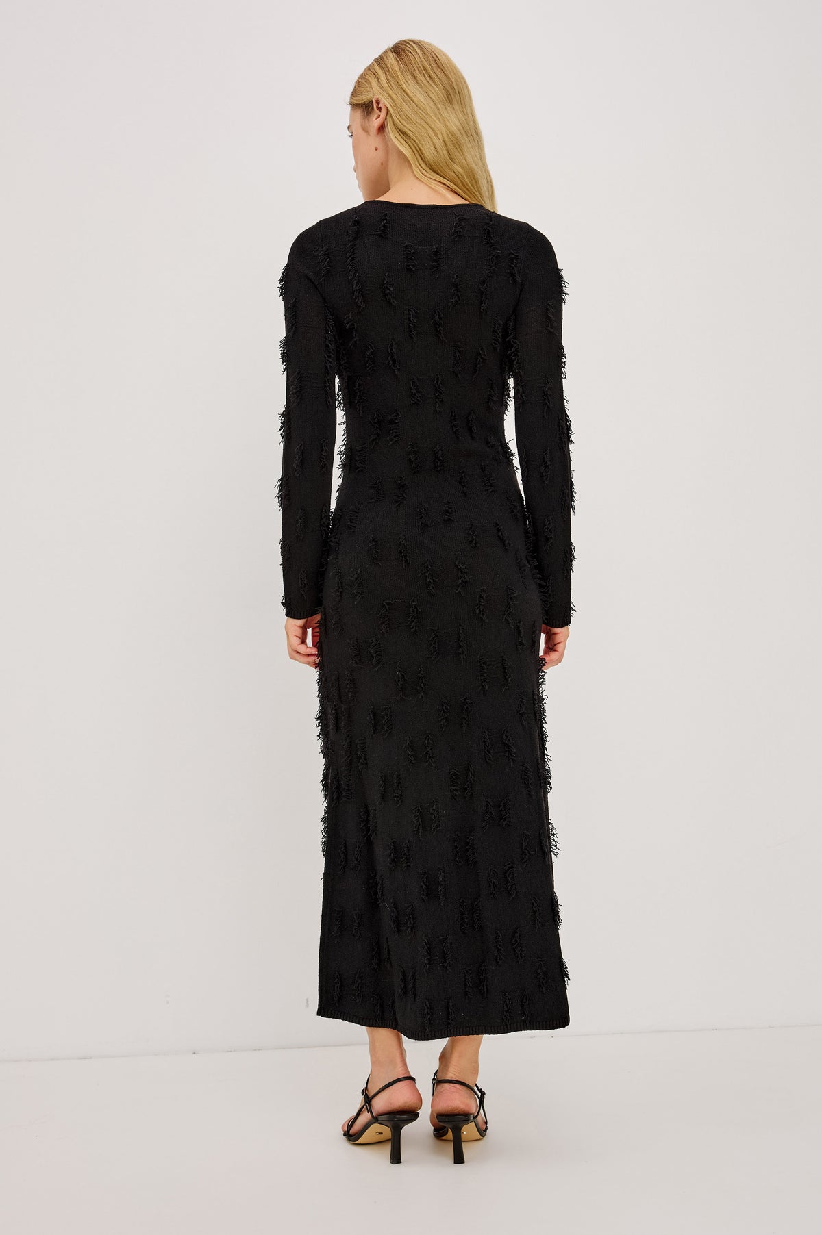 Sulma Maxi Dress Knit in Soft Fine-Gauge Yarn With Alover Fringe, Slim Fit Through Bodice and Long Sleeves, and A-Line Skirt in Black Colorway - Back Full Body View Featured on Model.