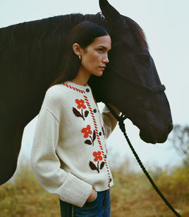 Woman in a floral sweater standing next to a horse in an outdoor setting