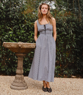 Woman in a gingham dress standing next to a stone fountain with greenery in the background