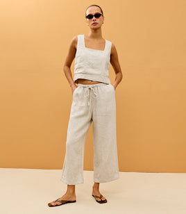 Woman wearing a beige sleeveless top and light-colored pants against an orange background