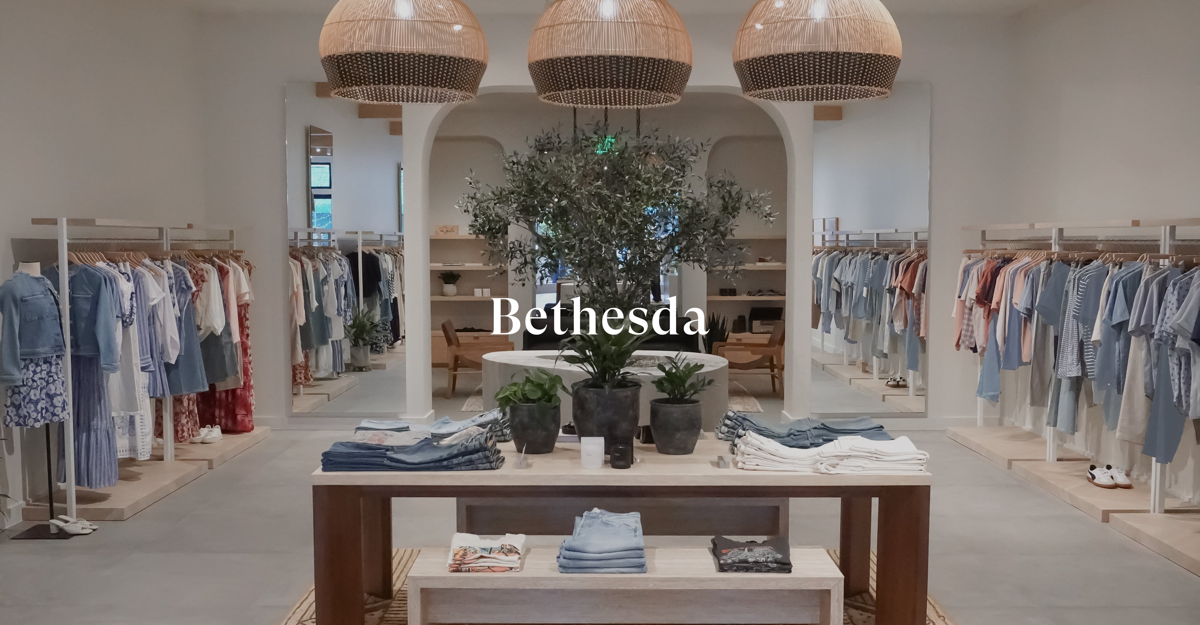 INSIDE OF BETHESDA STORE SHOWING MULTIPLE RACKS OF CLOTHING ALONG EACH WALL AND A TABLE IN THE CENTER OF THE ROOM