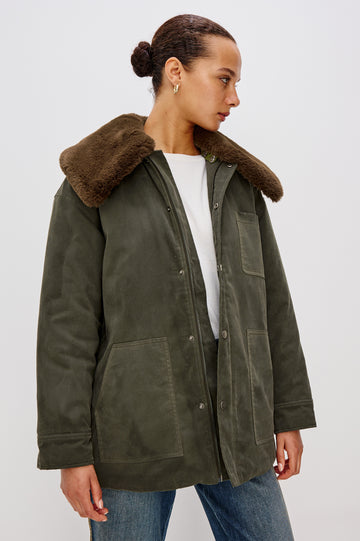 An umber waxed cotton canvas jacket with a removable vegan-fur collar. The jacket has a zip front with snap closures, quilted lining, chest patch pocket, and side pockets for a functional, workwear-inspired look. Front View Featured on Model.