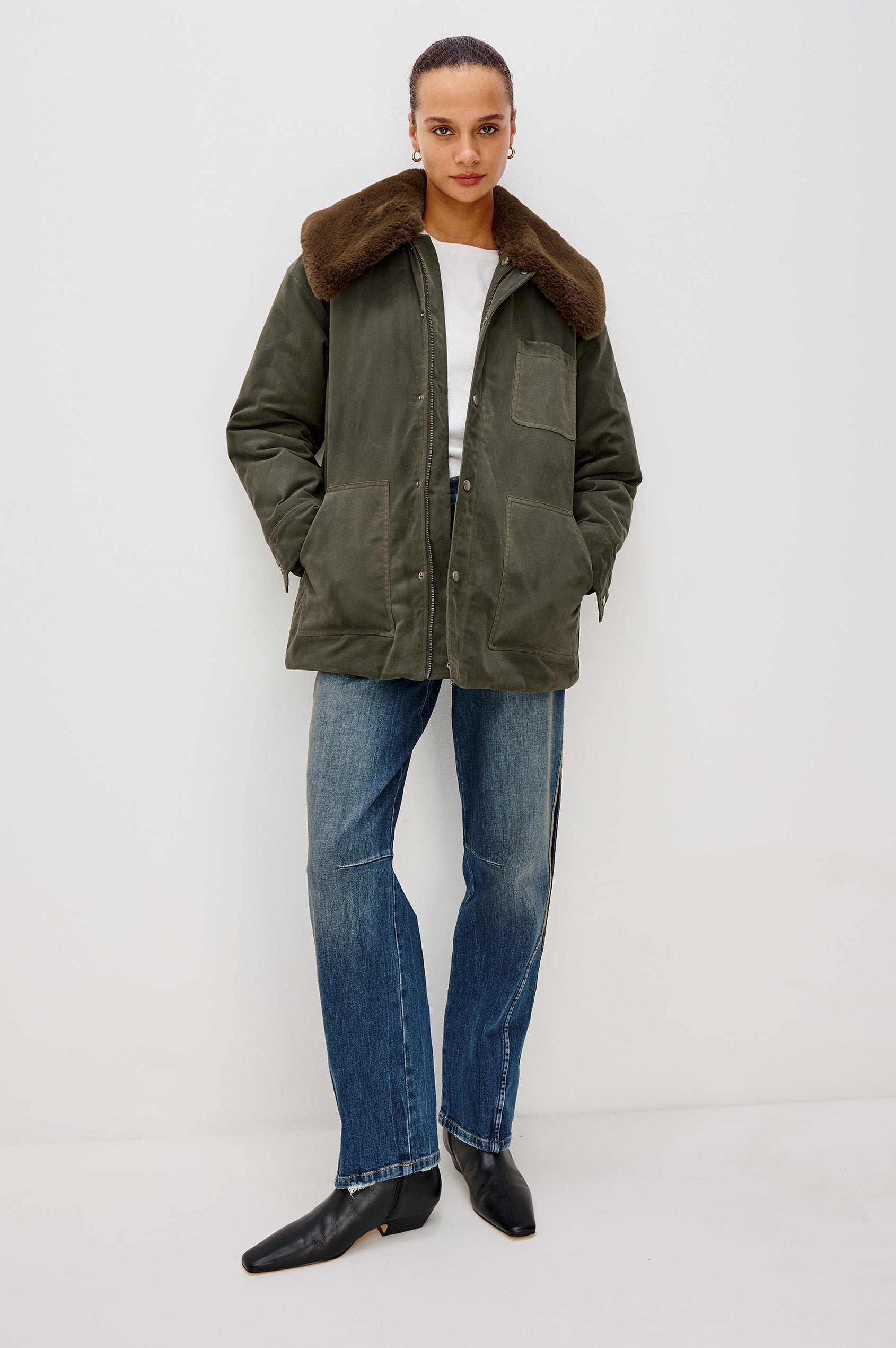 An umber waxed cotton canvas jacket with a removable vegan-fur collar. The jacket has a zip front with snap closures, quilted lining, chest patch pocket, and side pockets for a functional, workwear-inspired look. Full Body Front View Featured on Model.
