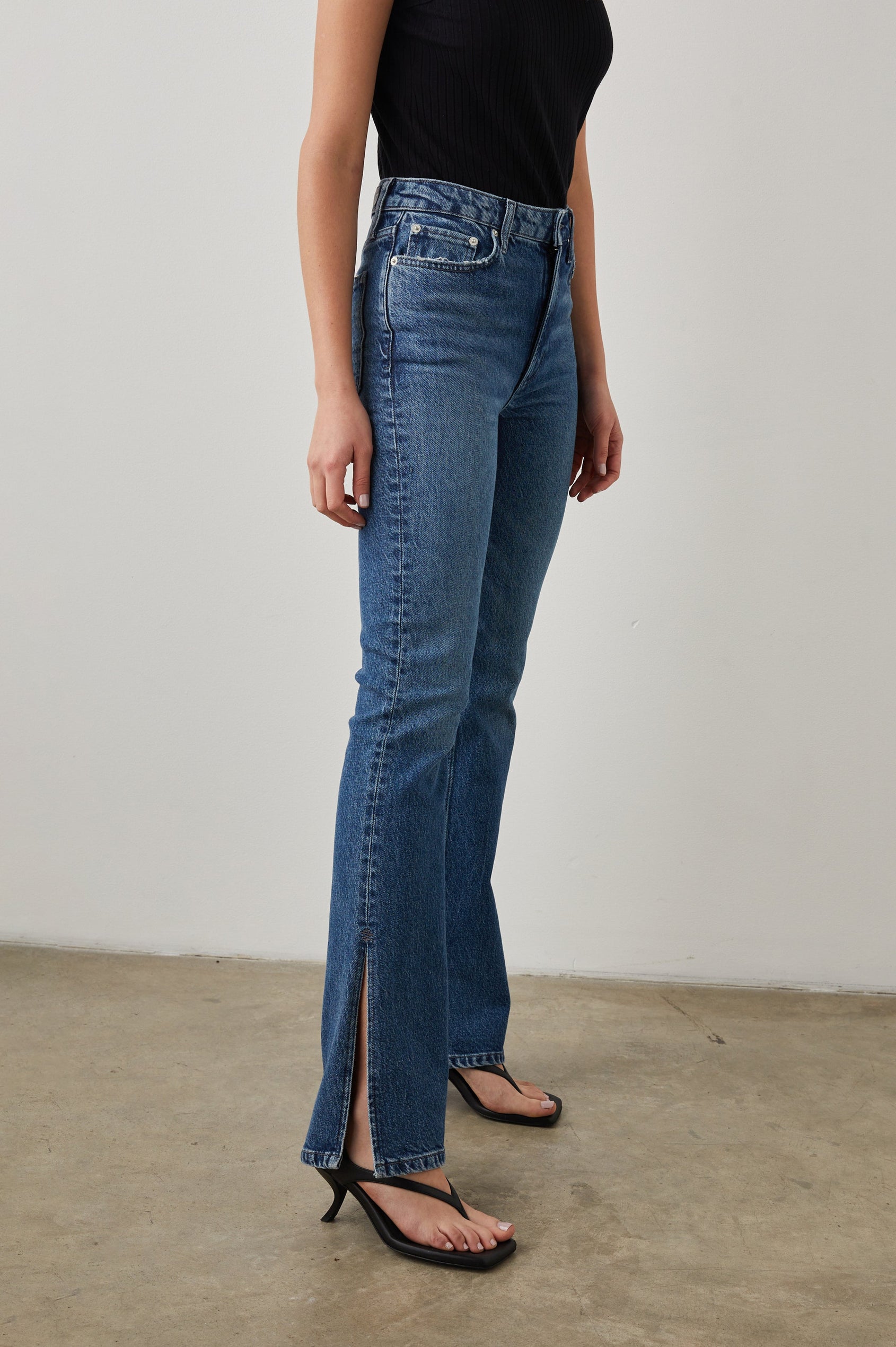 Sunset Crop Slim Fare Jeans with Outer Hem Slits, Belt Loops, Two Front Pockets plus a Coin Pocket and Two Back Patch Pockets in Navy Stone Colorway - Side View Featured on Model