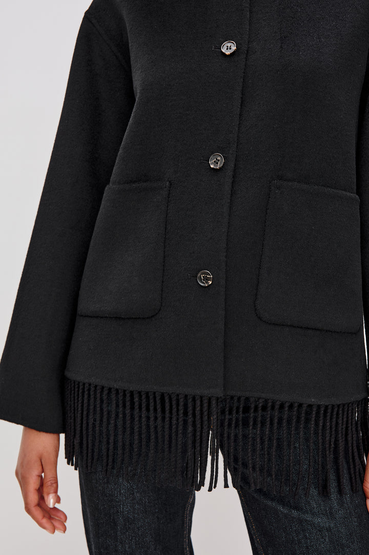 A heavyweight black wool-blend jacket with a relaxed fit. The jacket includes front button closures, patch pockets, and fringe detail at the hem for added texture and style. Close Up View Featured on Model.