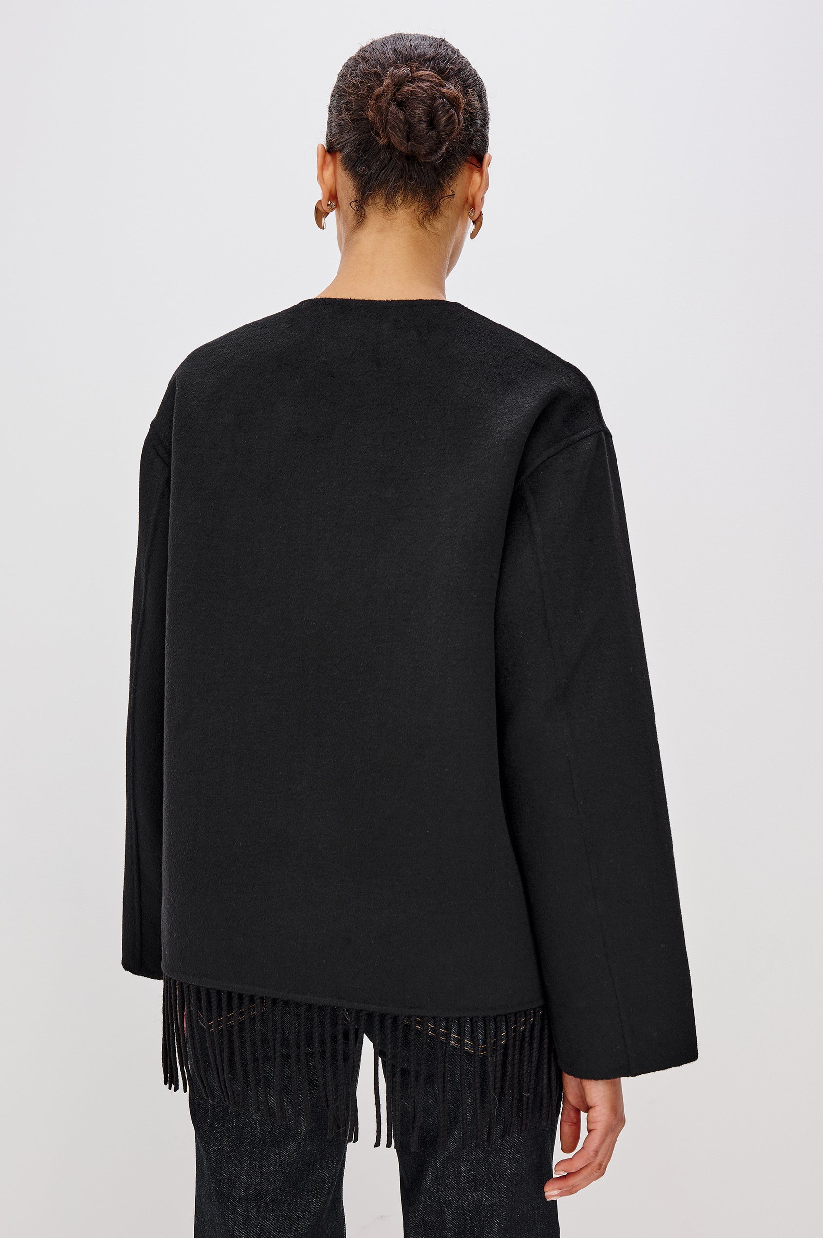 A heavyweight black wool-blend jacket with a relaxed fit. The jacket includes front button closures, patch pockets, and fringe detail at the hem for added texture and style. Back View Featured on Model.