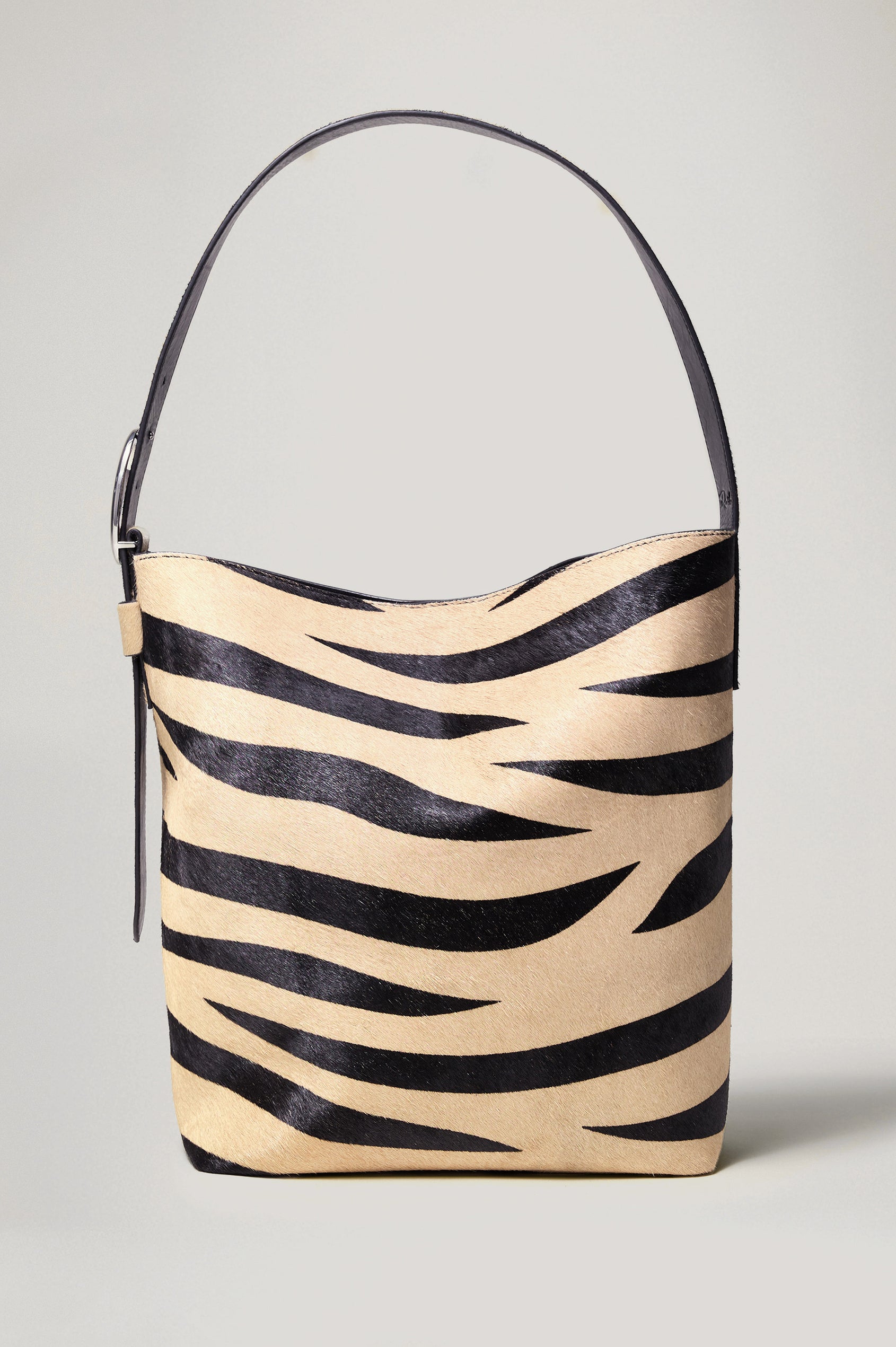 The Torino is a zebra-print haircalf leather bucket bag, designed with an adjustable strap and polished silver oval buckle. Front view featured.
