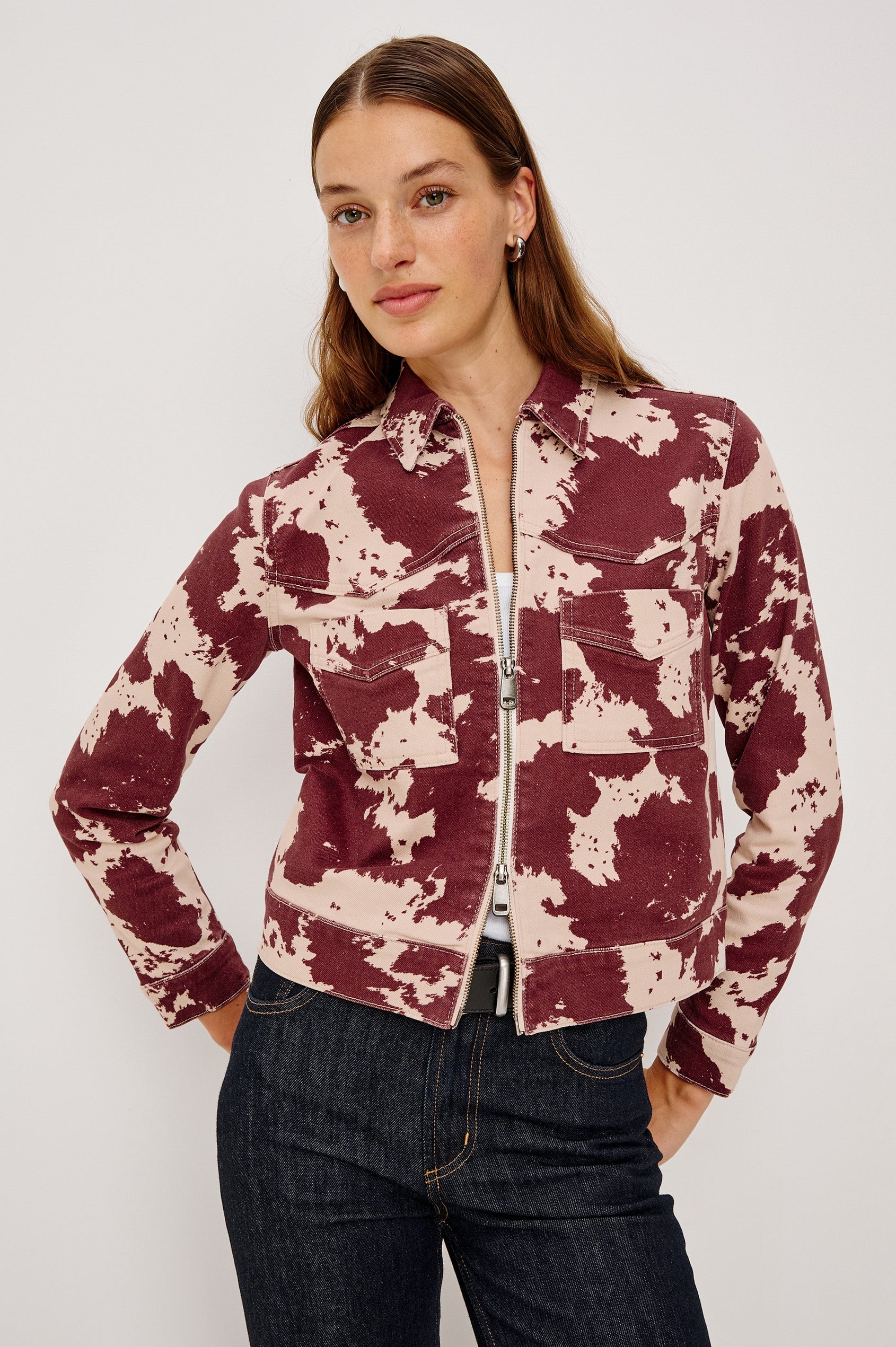 The Trabuco is a collared two-way zip front jacket with two chest pockets and a western style yoke in Cowgirl colorway - a red and beige cow print. Front view featured on model.