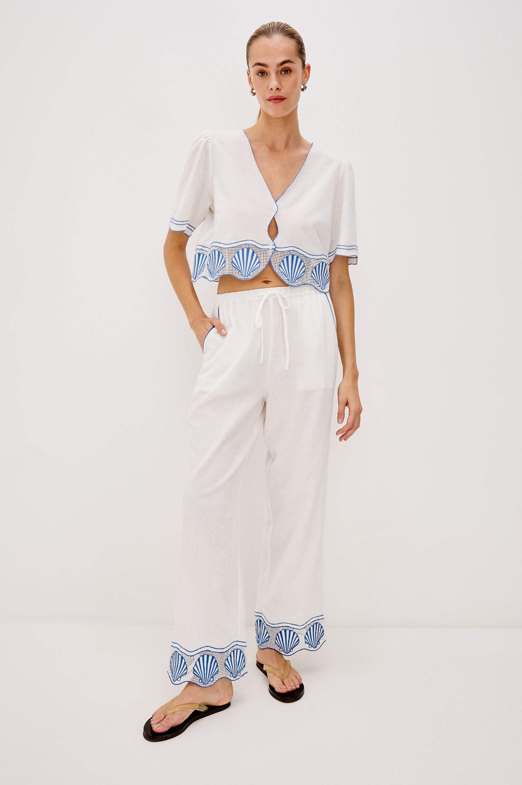 Venice Cropped V-Neck Top with Short Sleeves (slightly puffed), 2-Button Front, Keyhole at Center Front, Contrast Blue Sea Shell Embroidery and Scalloped Hem in White Colorway. Front Full Body View Shown on Model.