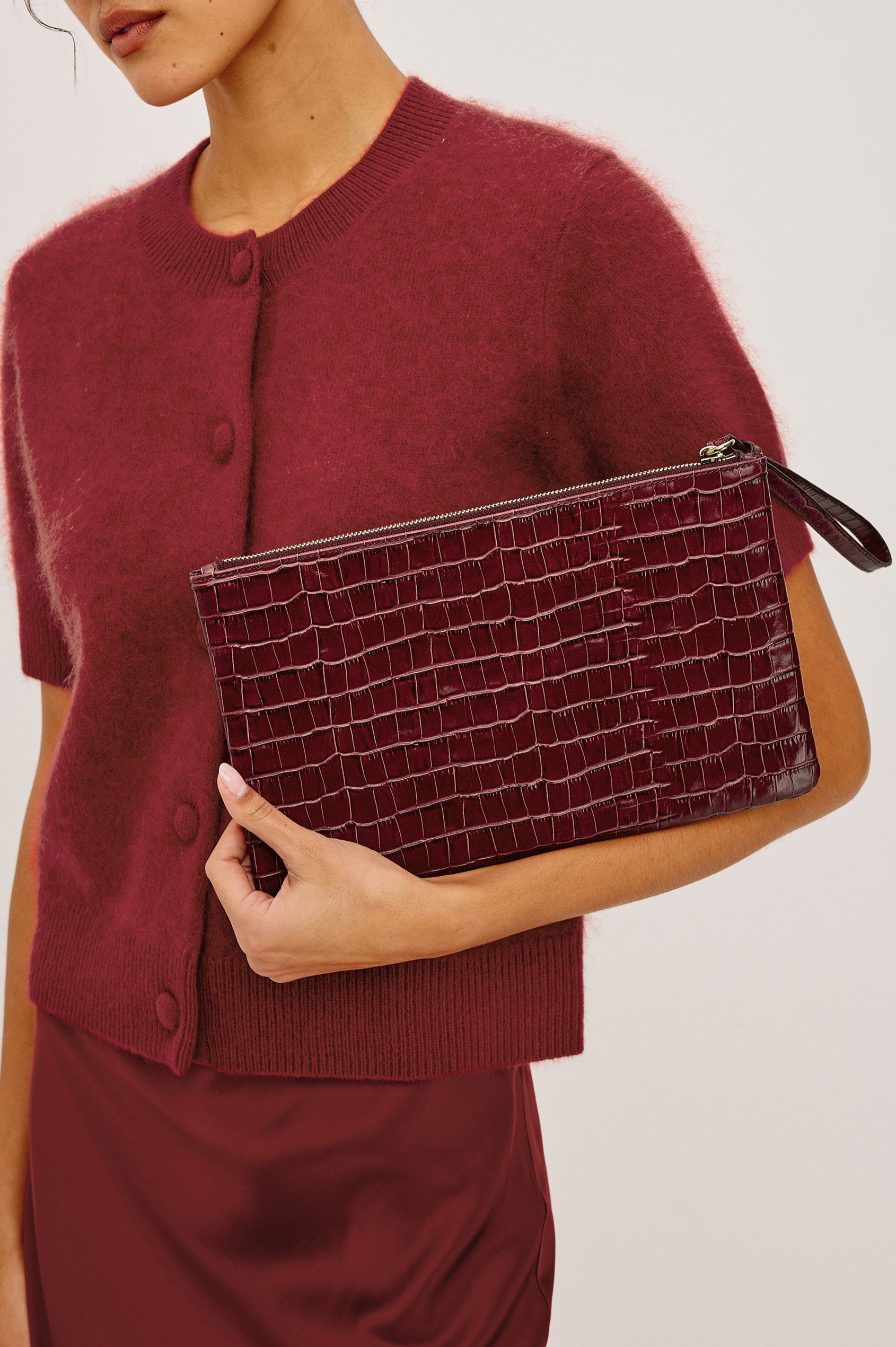 Verona Clutch Bag in Croc-Embossed Leather With Attached Wristlet Strap, Top Zip Closure, and Interior Slip Pocket in Burgundy Croc Embossed Colorway - Side View Featured on Model