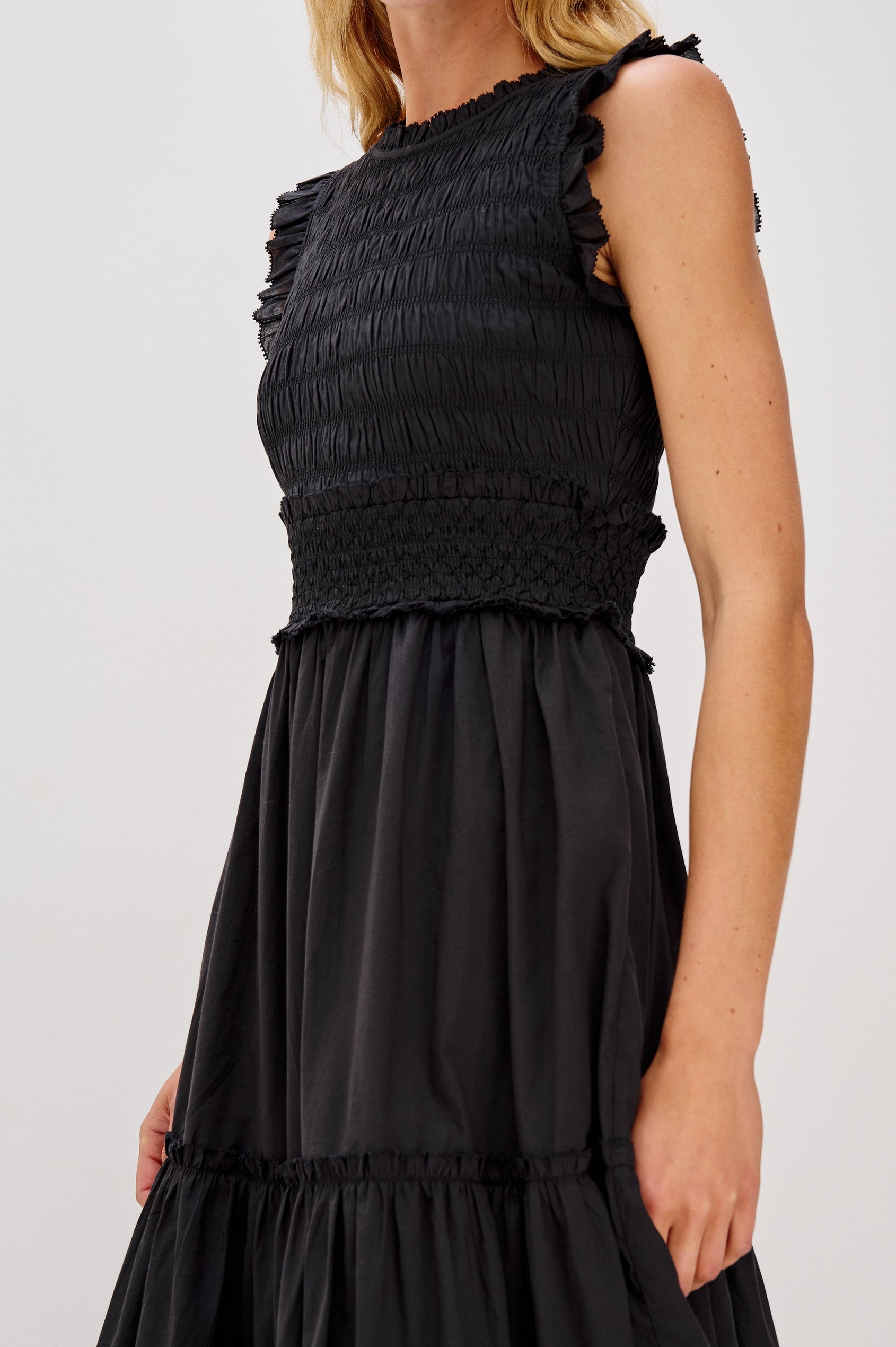 Vivier is a crinkled cotton poplin maxi dress featuring a smocked, fitted bodice and waistband. The dress flows into a relaxed skirt with soft ruffled tiers, creating a breezy silhouette in Black Colorway - Close up of Details on Model