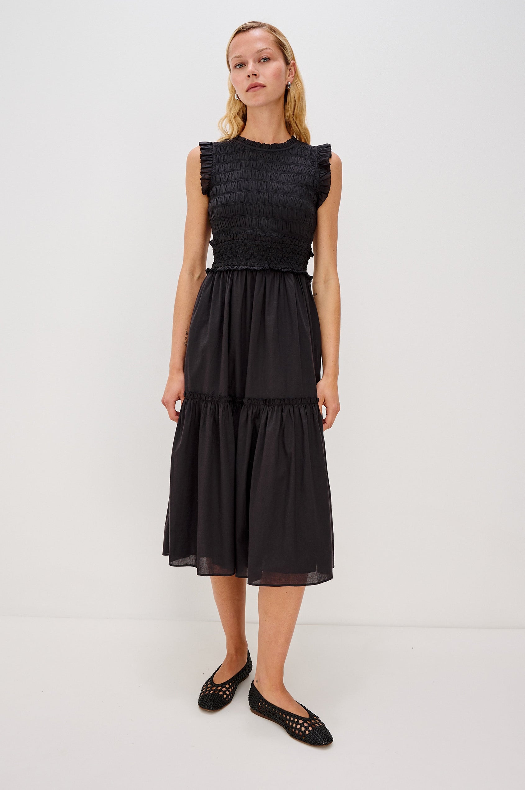 Vivier is a crinkled cotton poplin maxi dress featuring a smocked, fitted bodice and waistband. The dress flows into a relaxed skirt with soft ruffled tiers, creating a breezy silhouette in Black Colorway - Full Body Front View Featured on Model