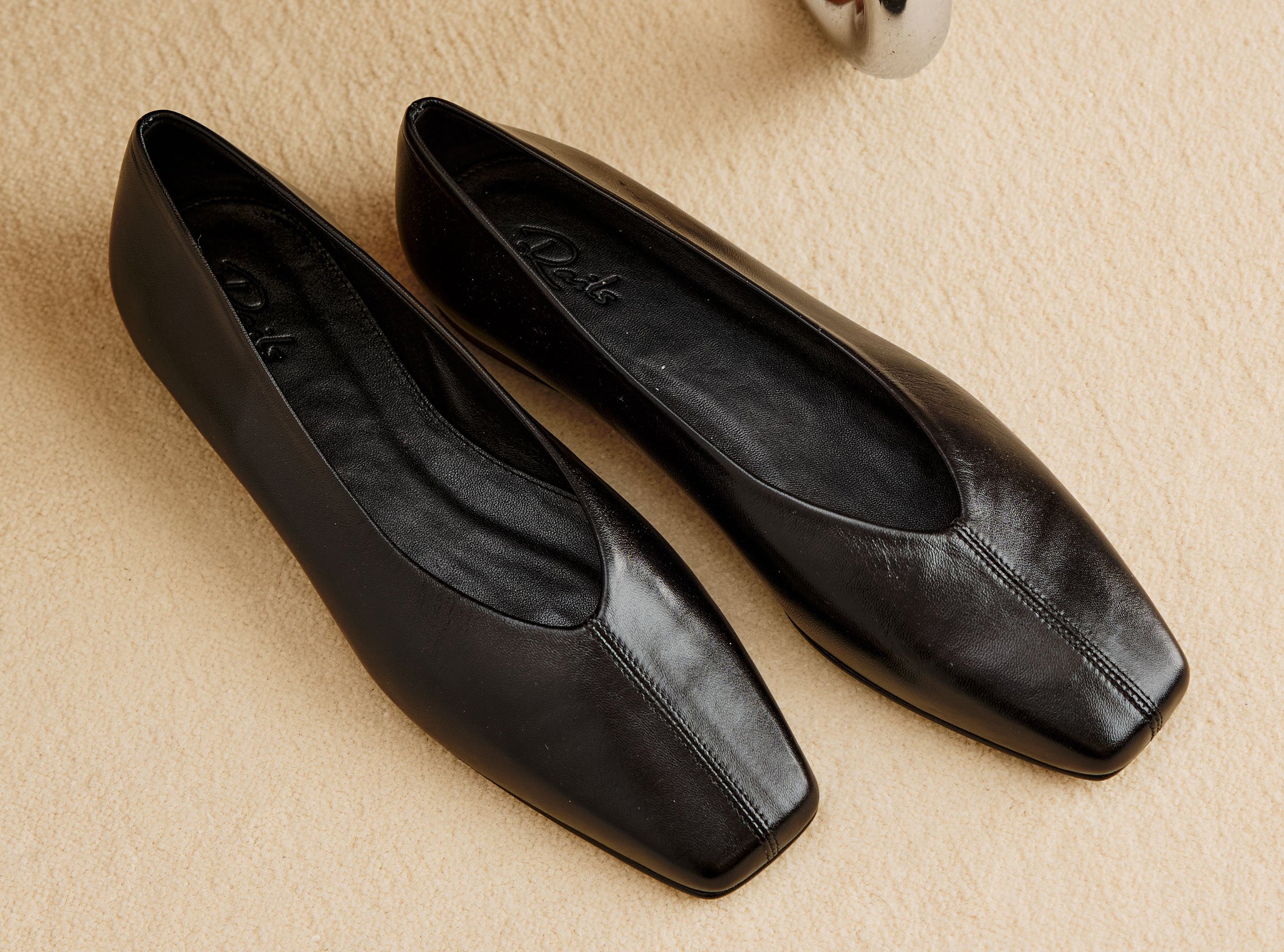Pair of black leather ballet flats displayed on a beige floor.