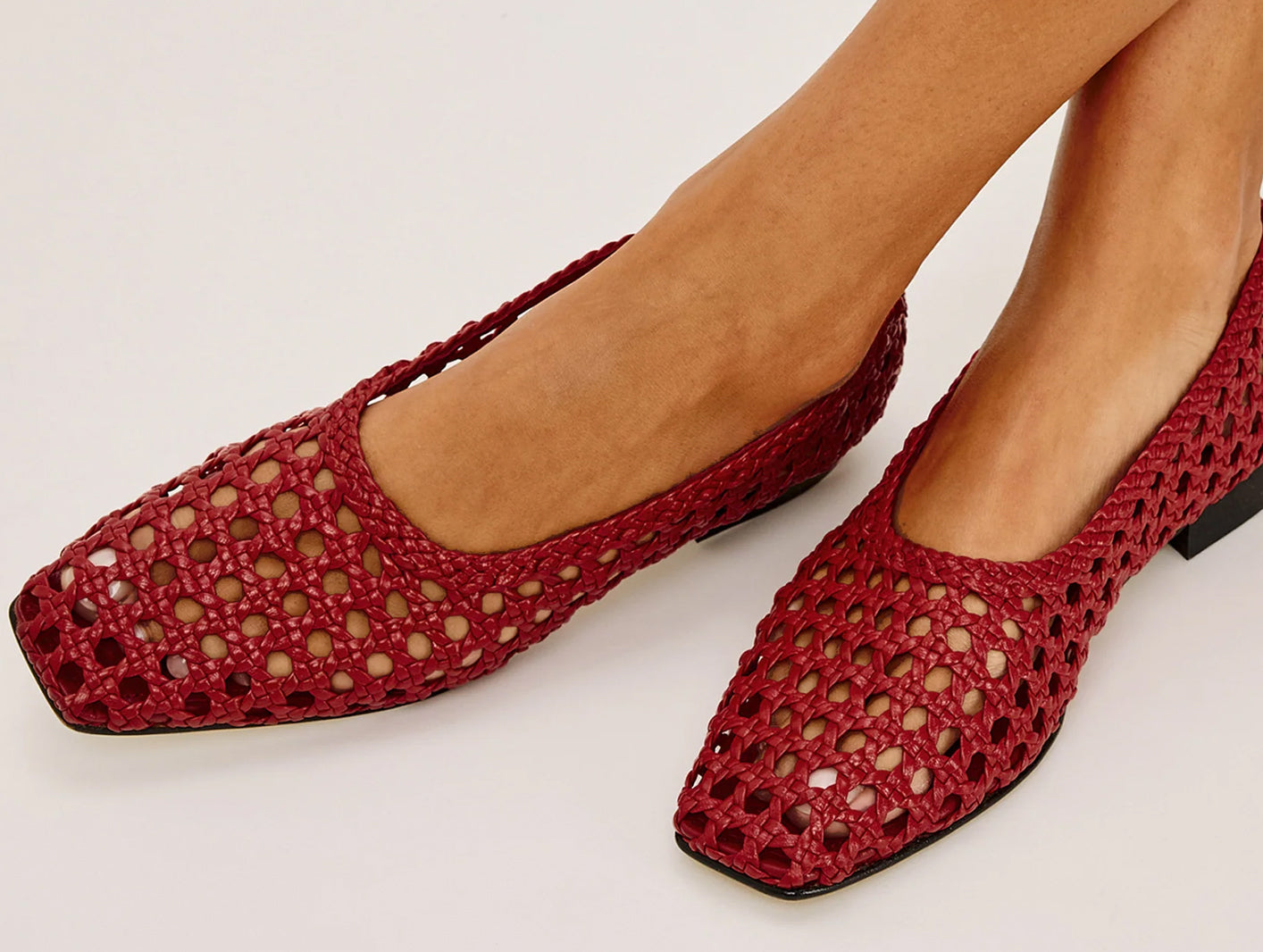 Red woven shoes worn by a person on a white background