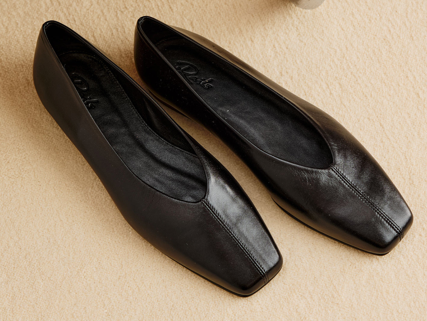 Pair of black leather ballet flats displayed on a beige floor.