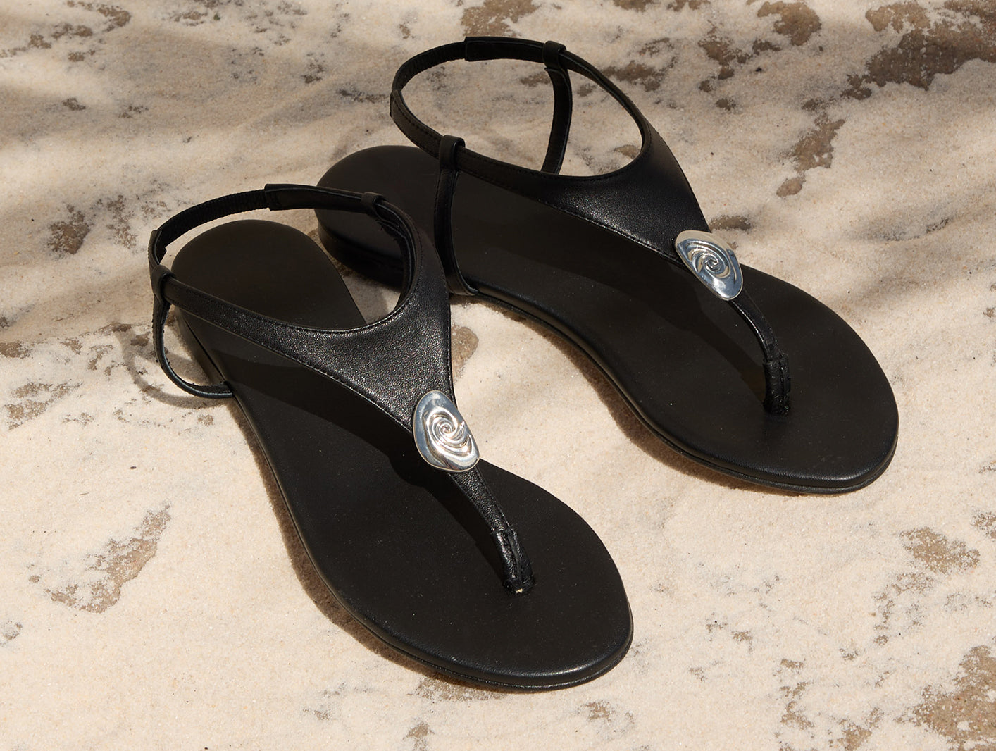 Black shoes with a silver emblem on the sandal