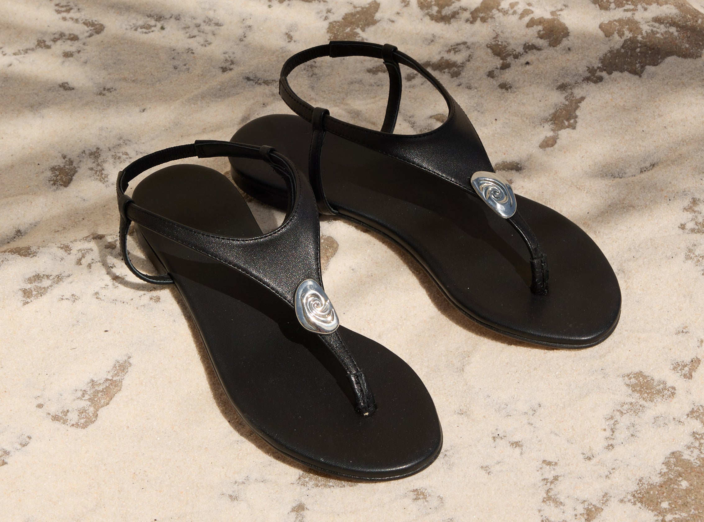Black shoes with a silver emblem on the sandal