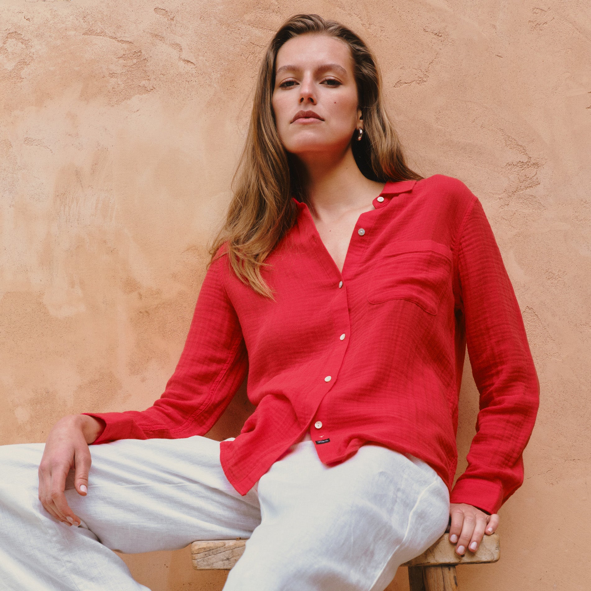 Woman wearing a red shirt sitting against a beige wall