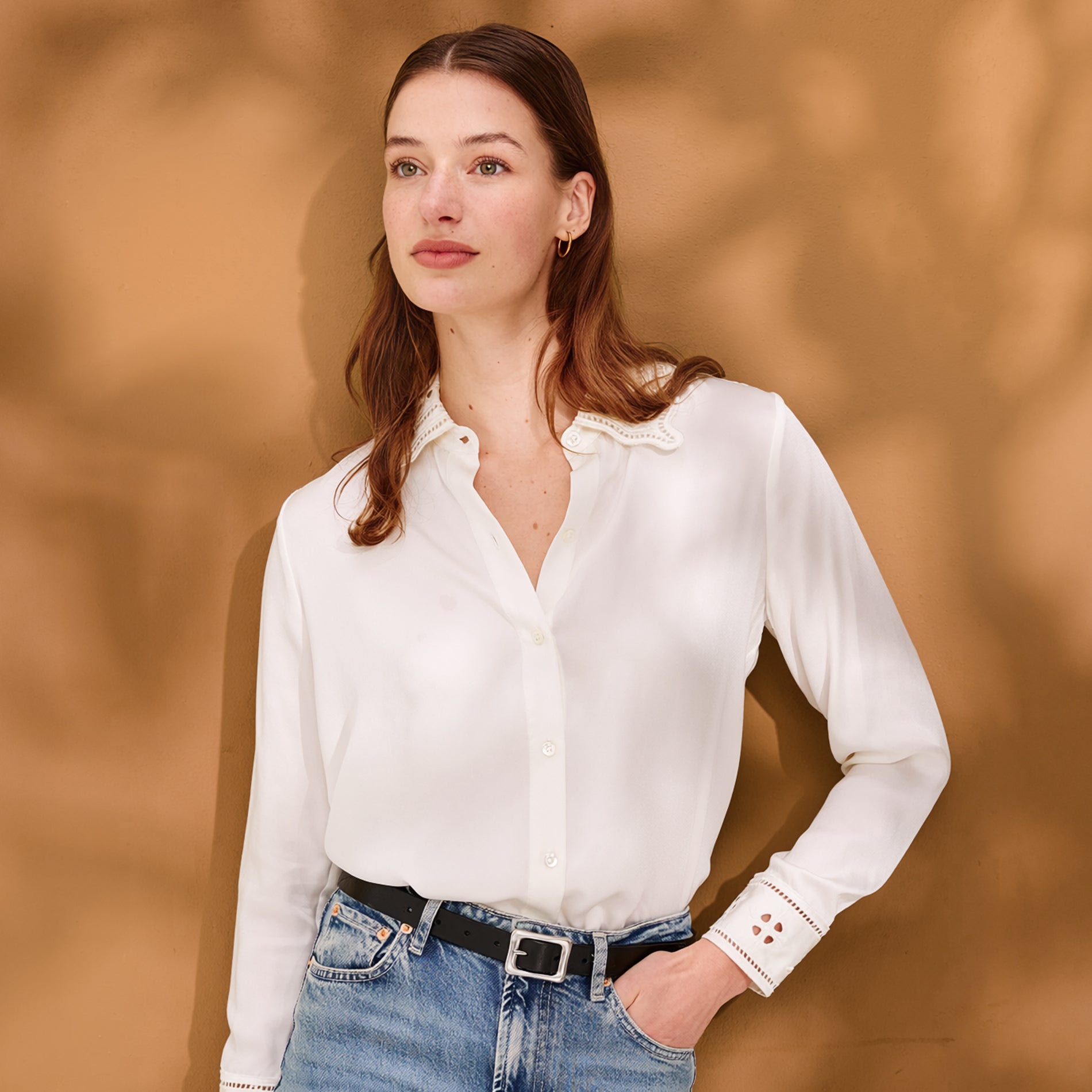 Woman wearing a white blouse and blue jeans against a warm brown background