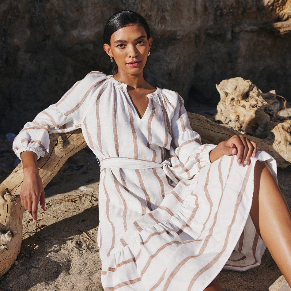 EDITORIAL IMAGE OF MODEL SITTING ON THE BEACH WEARING VITTORIA DRESS IN COCONUT STRIPE