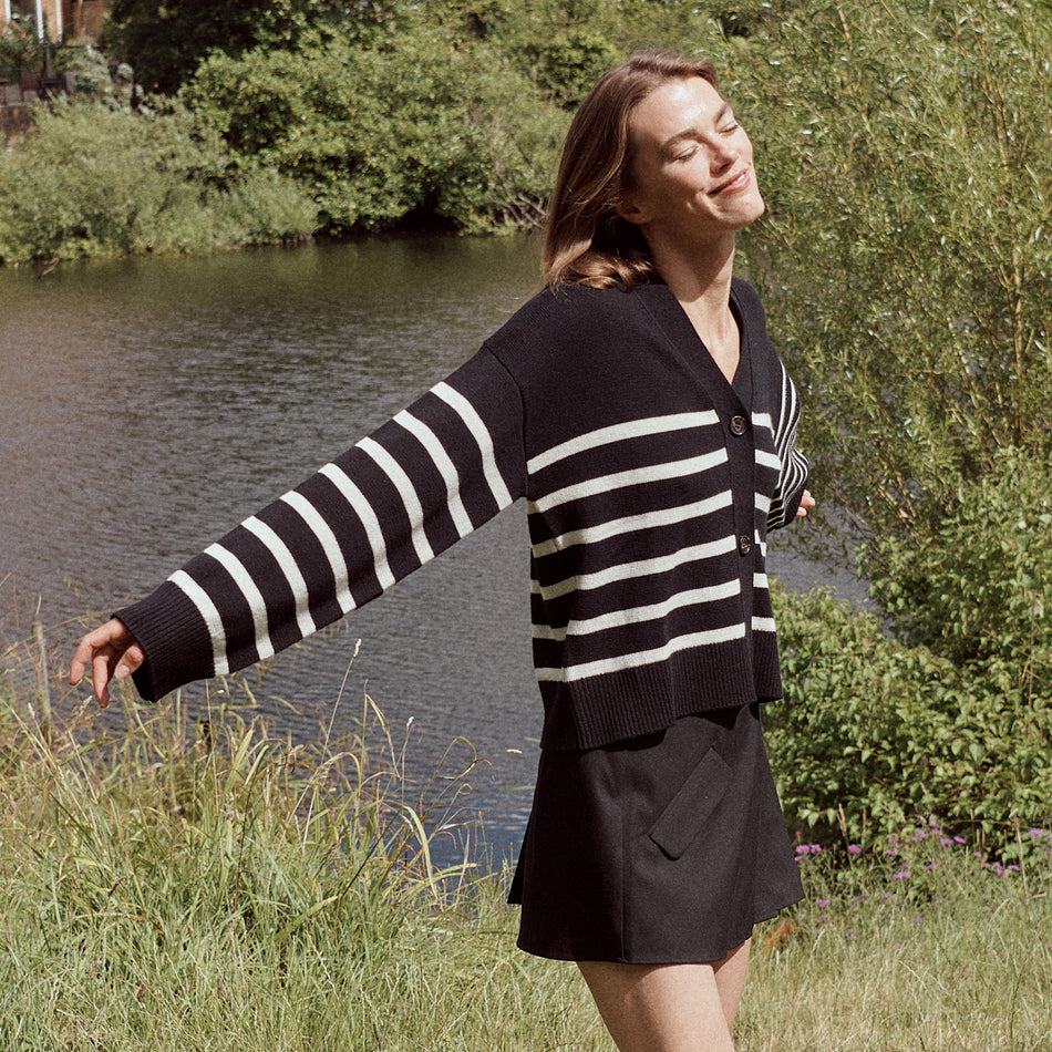 EDITORIAL IMAGE OF MODEL IN A FIELD WEARING GENEVA SWEATER IN BLACK OATMEAL STRIPES