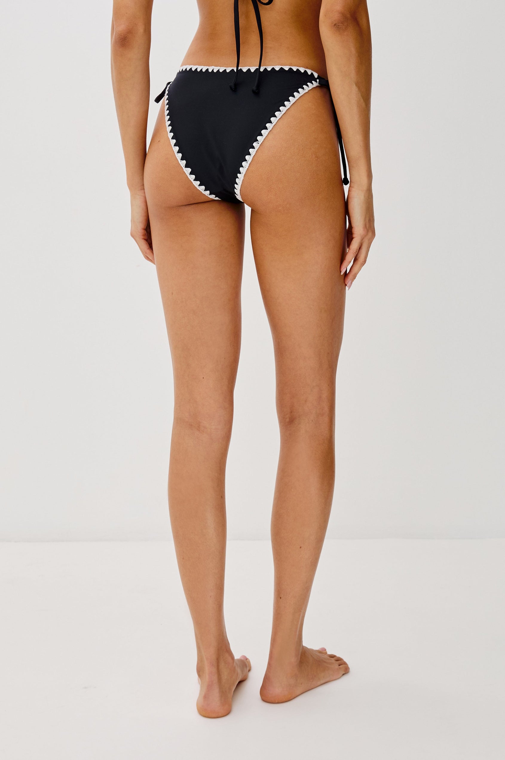 Zahra Mid Rise Bikini Bottom with a Tie Side, Classic Coverage and Contrast White Blanket Stitch at Seams in Black Colorway. Back View Shown on Model.