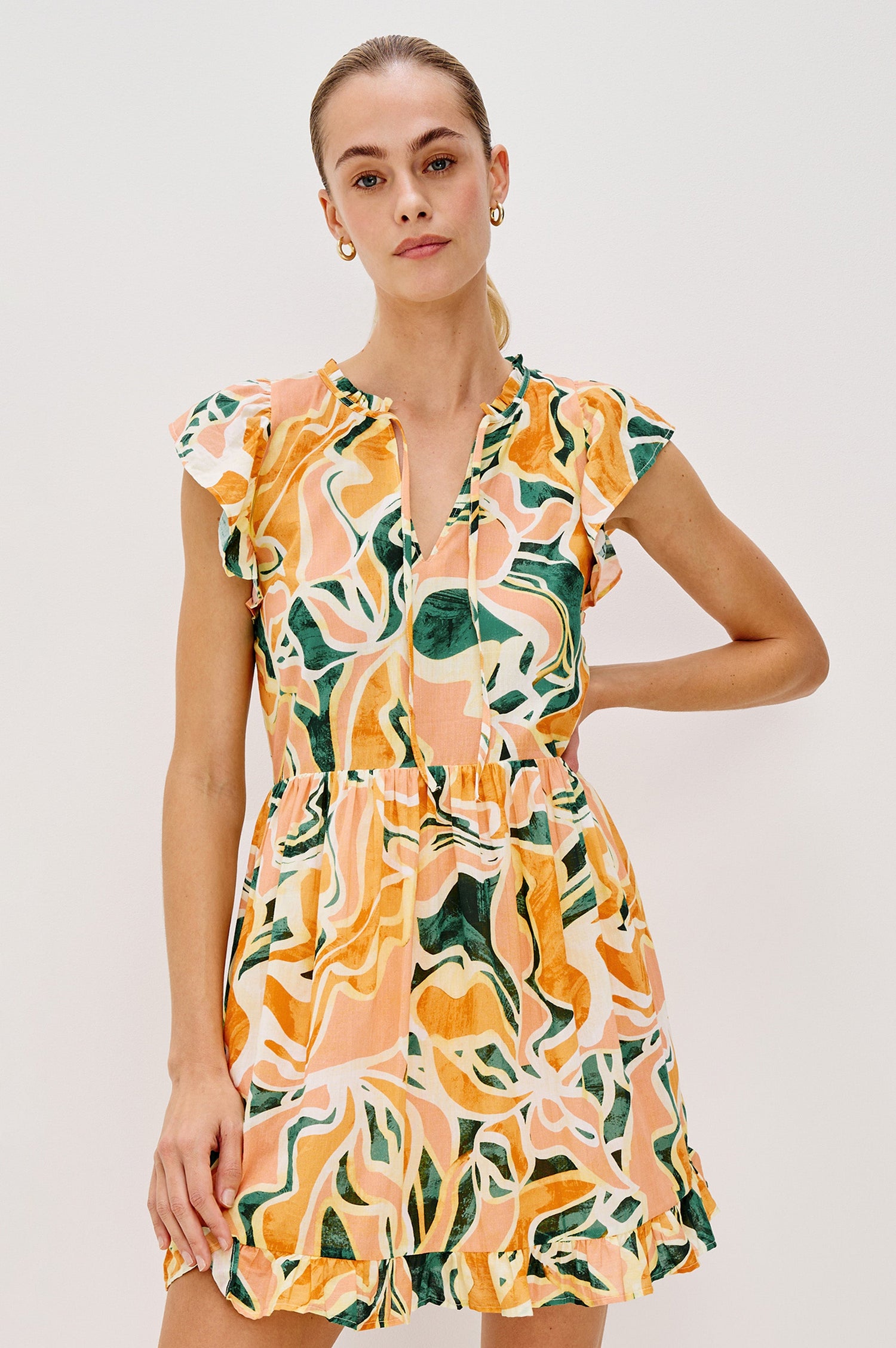 Zinnia Popover Mini Dress with Short Flutter Sleeves, Small Ruffle at Neck, V-Front with Self Tie Closure, Ruffle Hem in Tulum Colorway. Front View Shown on Model.