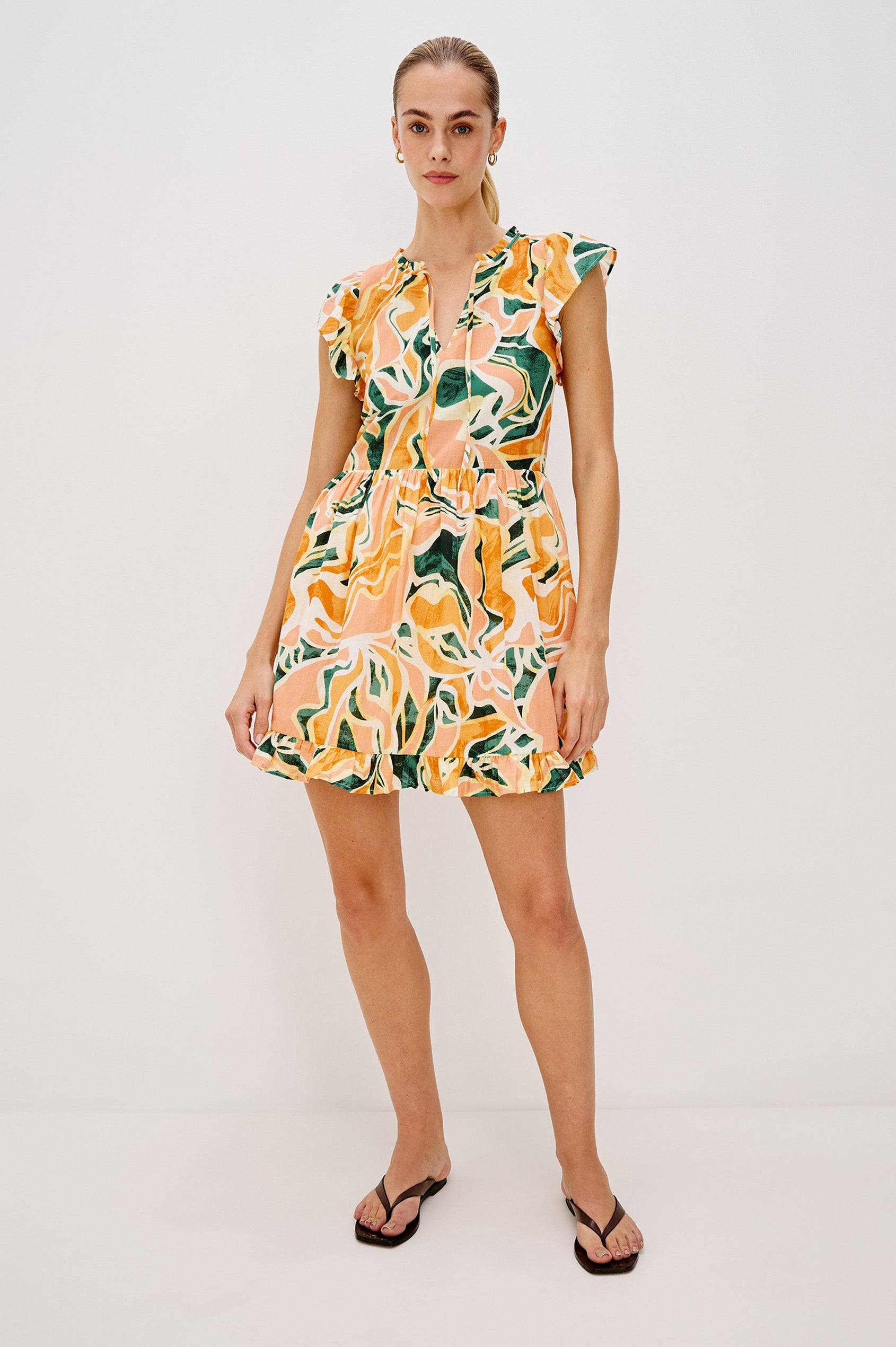Zinnia Popover Mini Dress with Short Flutter Sleeves, Small Ruffle at Neck, V-Front with Self Tie Closure, Ruffle Hem in Tulum Colorway. Full Body Front View Shown on Model.
