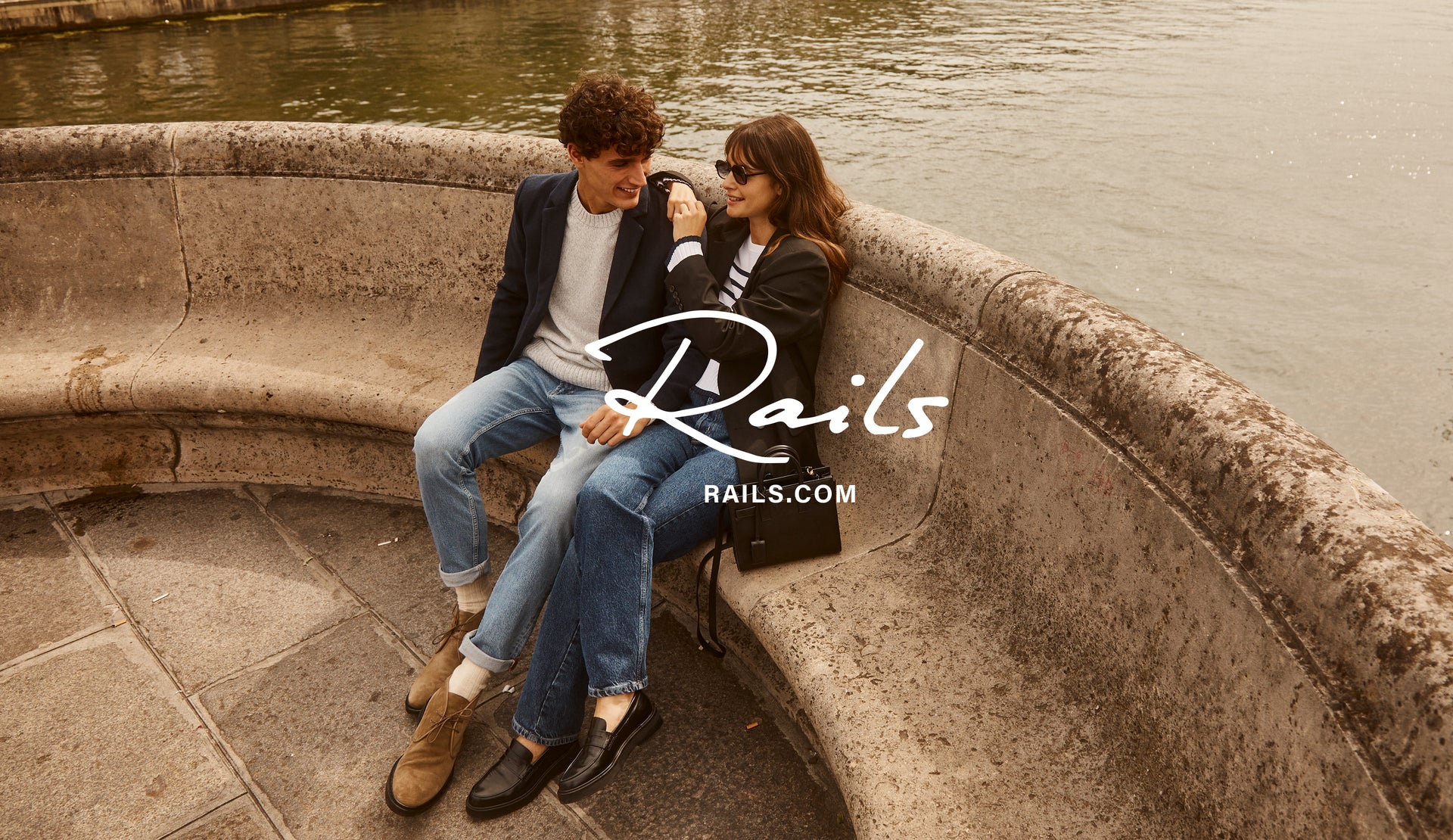 EDITORIAL IMAGE OF TWO MODELS SITTING. FIRST MODEL IS WEARING LARK COAT, DONOVAN SWEATER, AND CLAYTON SLIM STRAIGHT JEAN. SECOND MODEL IS WEARING JAC BLAZER, GEMMA SWEATER, AND TOPANGA STRAIGHT JEAN.