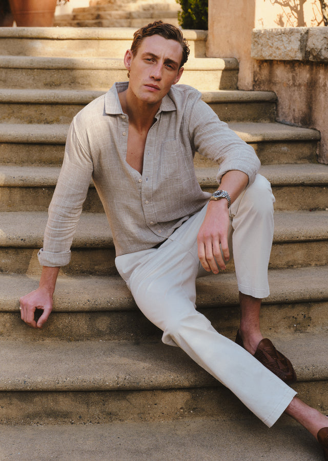 Man sitting on stone steps wearing a beige shirt and white pants.