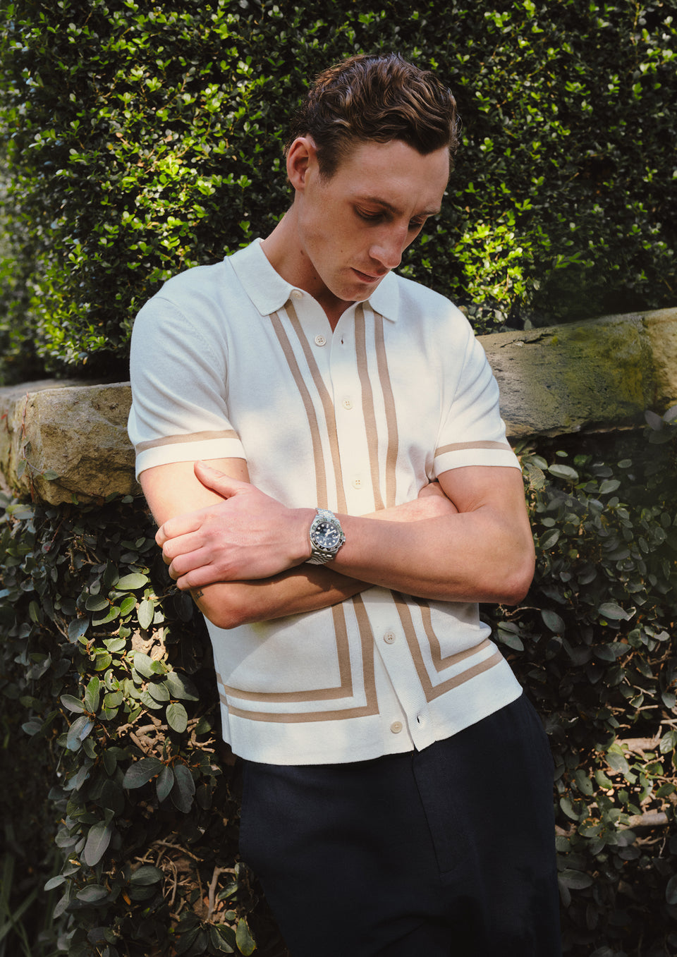 Man wearing a white shirt with brown accents against a green foliage background